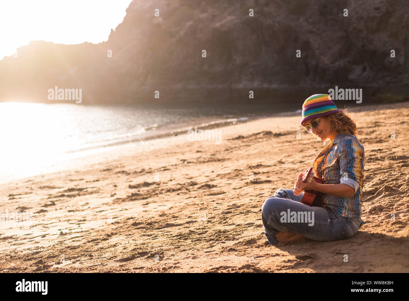 Schöne und ruhige junge Frau sitzt am Ufer am Strand anjoying Freizeitaktivitäten Aktivität auf dem Sand spielen eine ukulele Gitarre in der Nähe des Ozeans für Urlaub und Freiheit Konzept lächelnd Stockfoto Schöne und ruhige junge Frau sitzt am Ufer am Strand anjoying Freizeitaktivitäten Aktivität auf dem Sand spielen eine ukulele Gitarre in der Nähe des Ozeans für Urlaub und Freiheit Konzept lächelnd Stockfoto