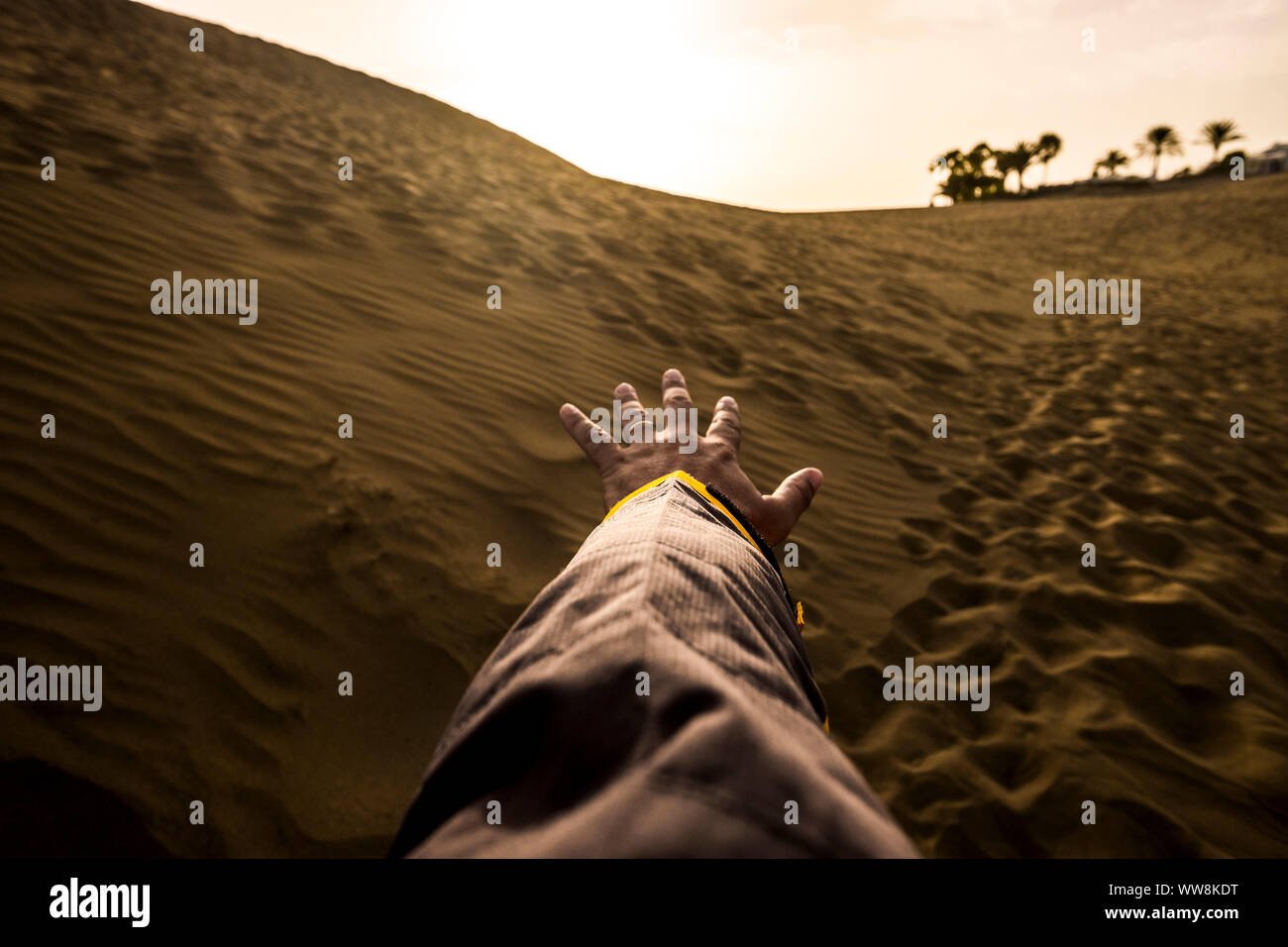 Hand und männlichen Arm bereit zu berühren und den Horizont in der dürren Wüste, ohne Wasser. oeasis im Hintergrund. Dünen und Sand und Footprint von Menschen auf dem Boden. Licht und Schatten und Konzept für einsame Mann erkunden Stockfoto