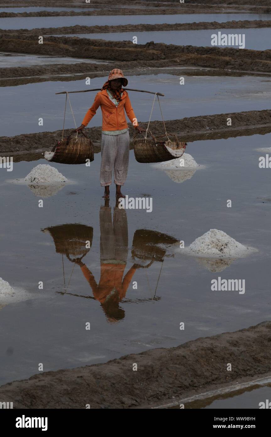 Reflexion eines Salzes Arbeiter tragen Rattankörbe beladen w/geerntete Salz in die Salzfelder, Kampot Province, Kambodscha. © kraig Lieb Stockfoto
