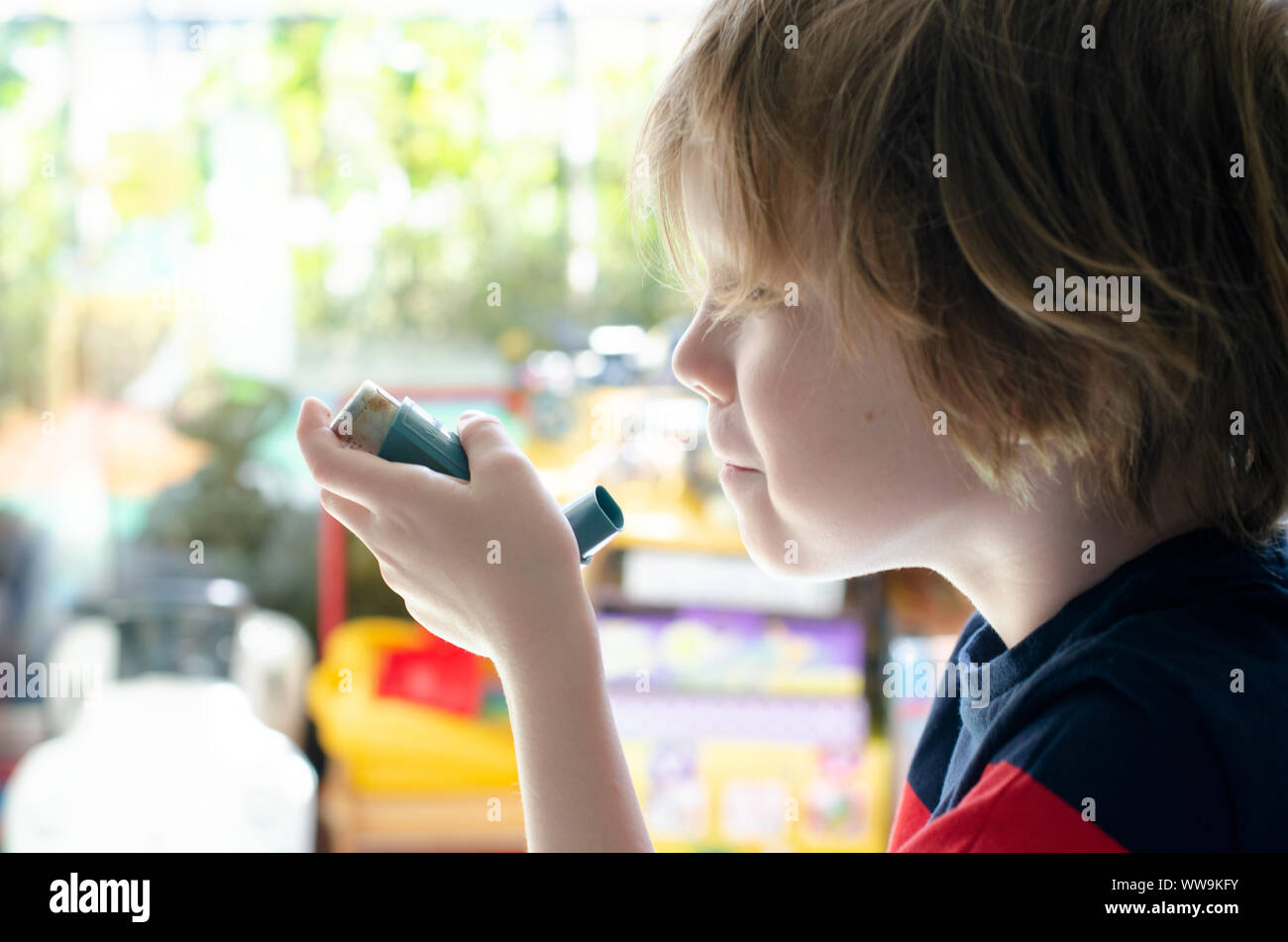 Vereinigtes Königreich, 10. Juli 2019: kleiner Junge vor einem Fenster mit einem Ventolin inhaler Stockfoto