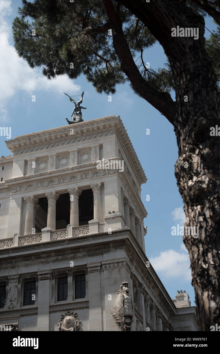 Rom, Italien, 5. Juli 2018: Ein Baum Frames eine reich verzierte Gebäude mit eine geflügelte Statue auf einem Sommertag in Rom gekrönt. Stockfoto