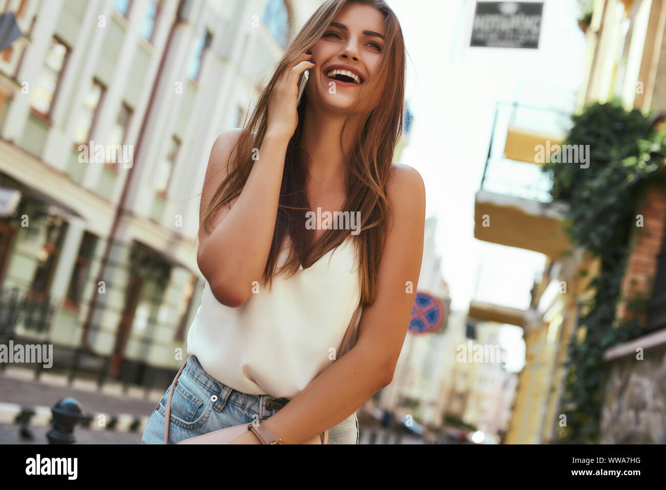 Porträt der jungen stilvolle Frau lächelnd beim Gehen auf die Straße, mit niedlichen trendy Outfit. Sie spricht am Telefon mit einer Freundin. Sommer lifestyle Konzept. Horizontale Schuß Stockfoto