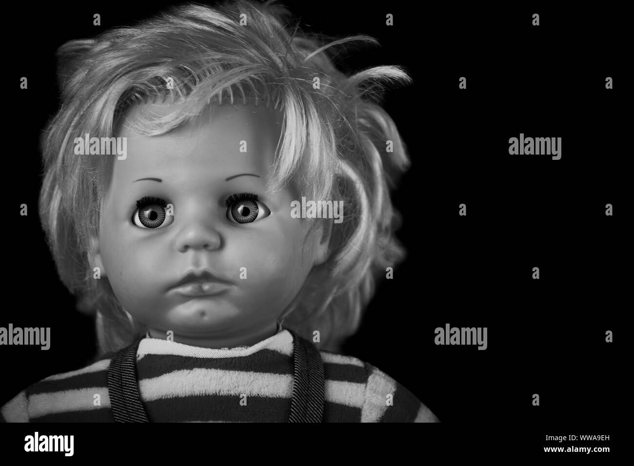 Gruseliger Puppenkopf in schwarz und weiß. Ein gruseliges Gesicht einer seltsamen Vintage-Puppe auf schwarzem Hintergrund isoliert Stockfoto