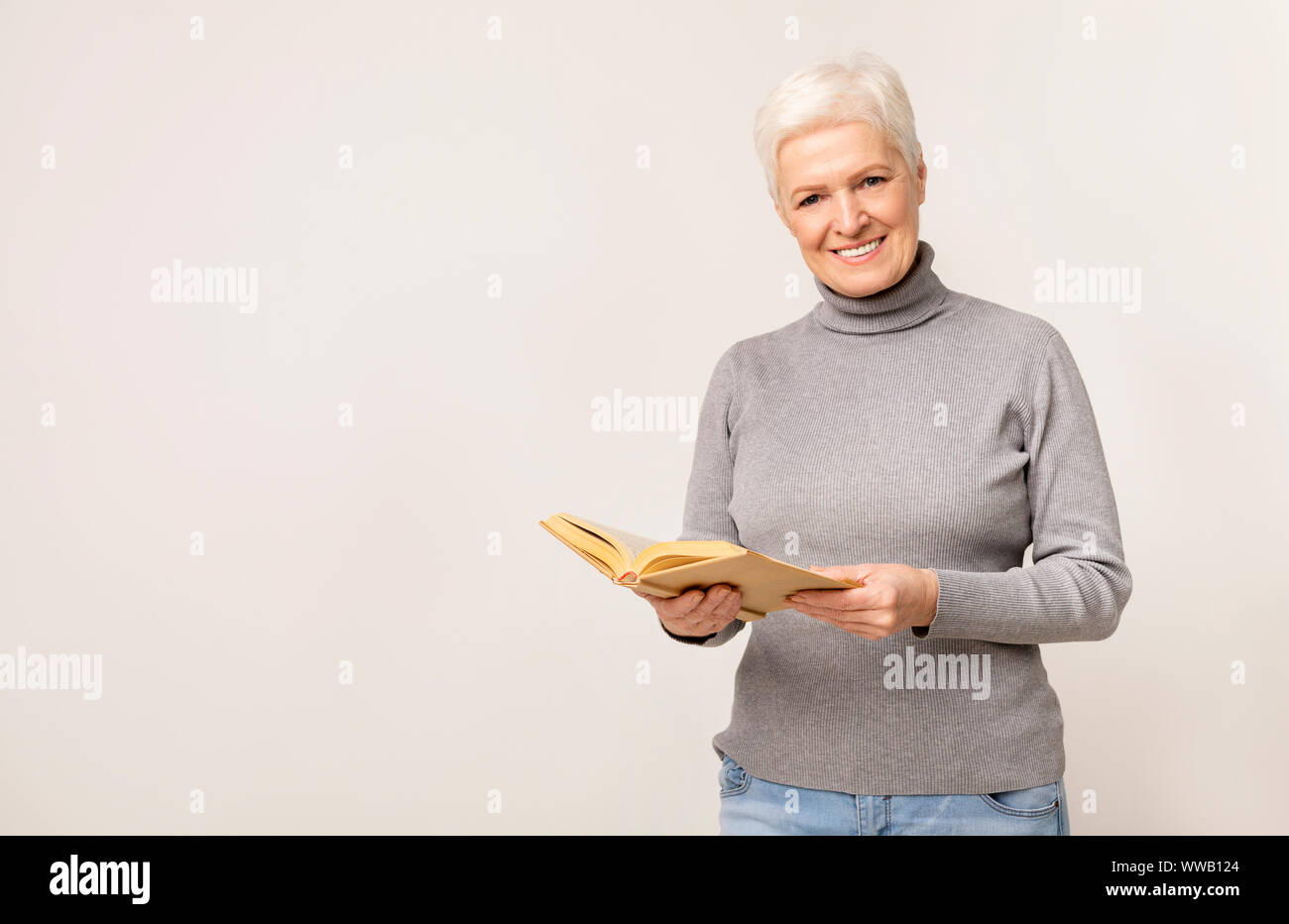 Schöne ältere Dame holding Buch und lächelnd in die Kamera Stockfoto