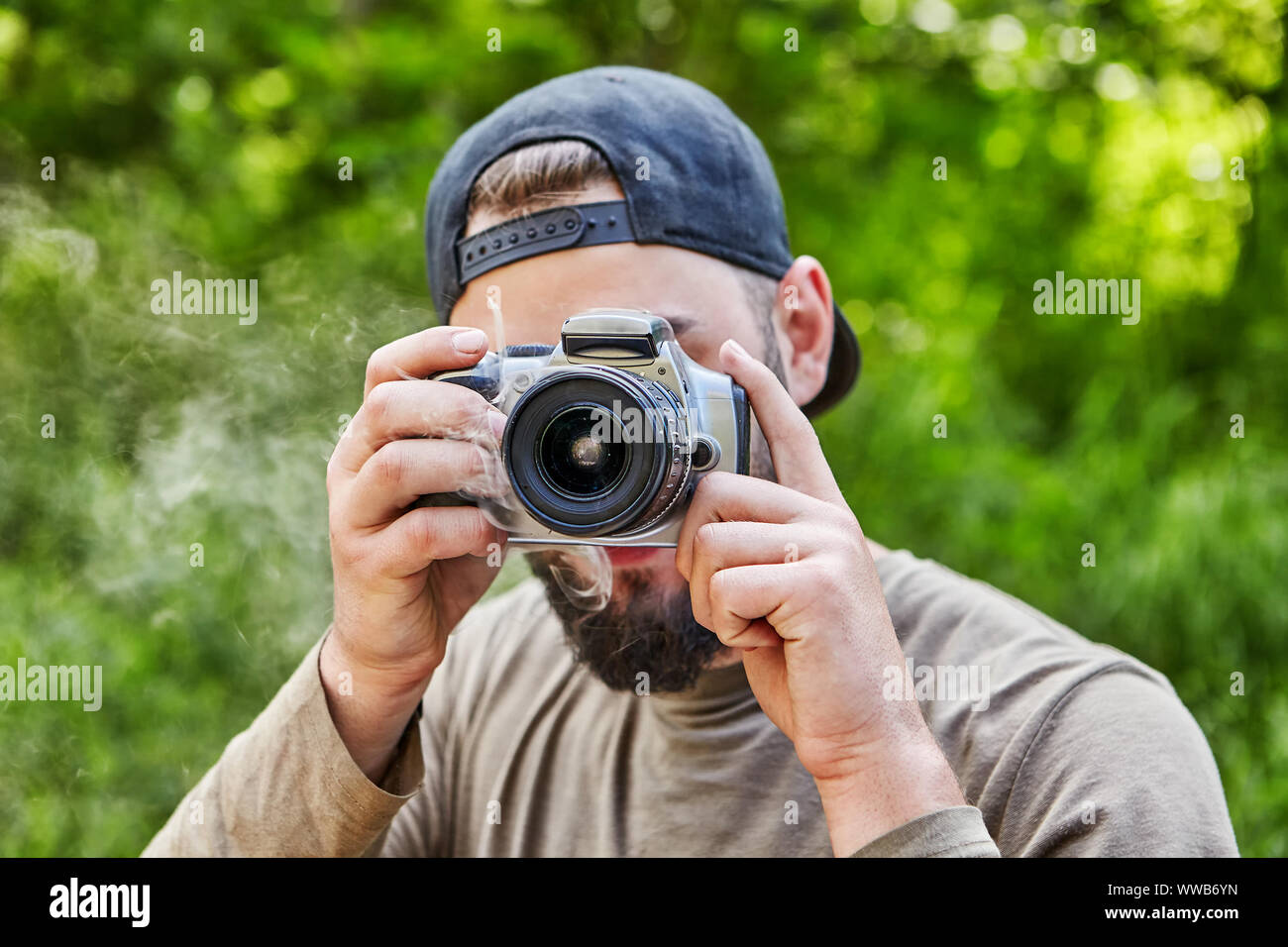 Die Kamera raucht in den Händen eines jungen Bartgeier Fotograf in einem Baseball Cap, Visor, der ein Foto in die Natur nimmt. Ein männlicher Photographe Stockfoto