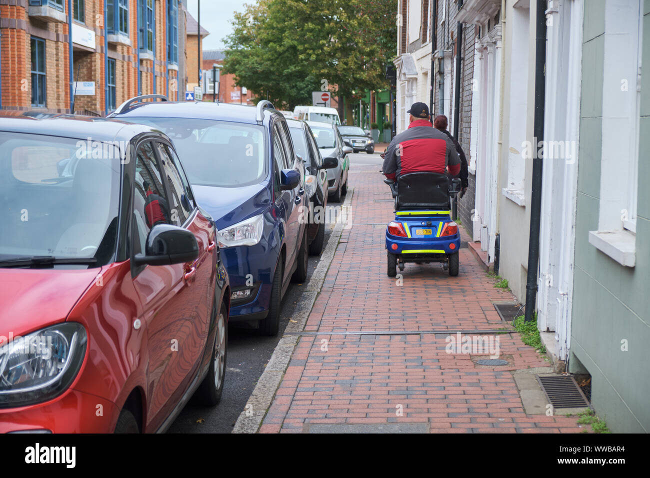 Person eingeschränkter Mobilität auf elektrischer Roller fahren auf schmalen Bürgersteig von einer Fußgängerzone vor verlangsamt. Lewes, UK, September 2019 Stockfoto