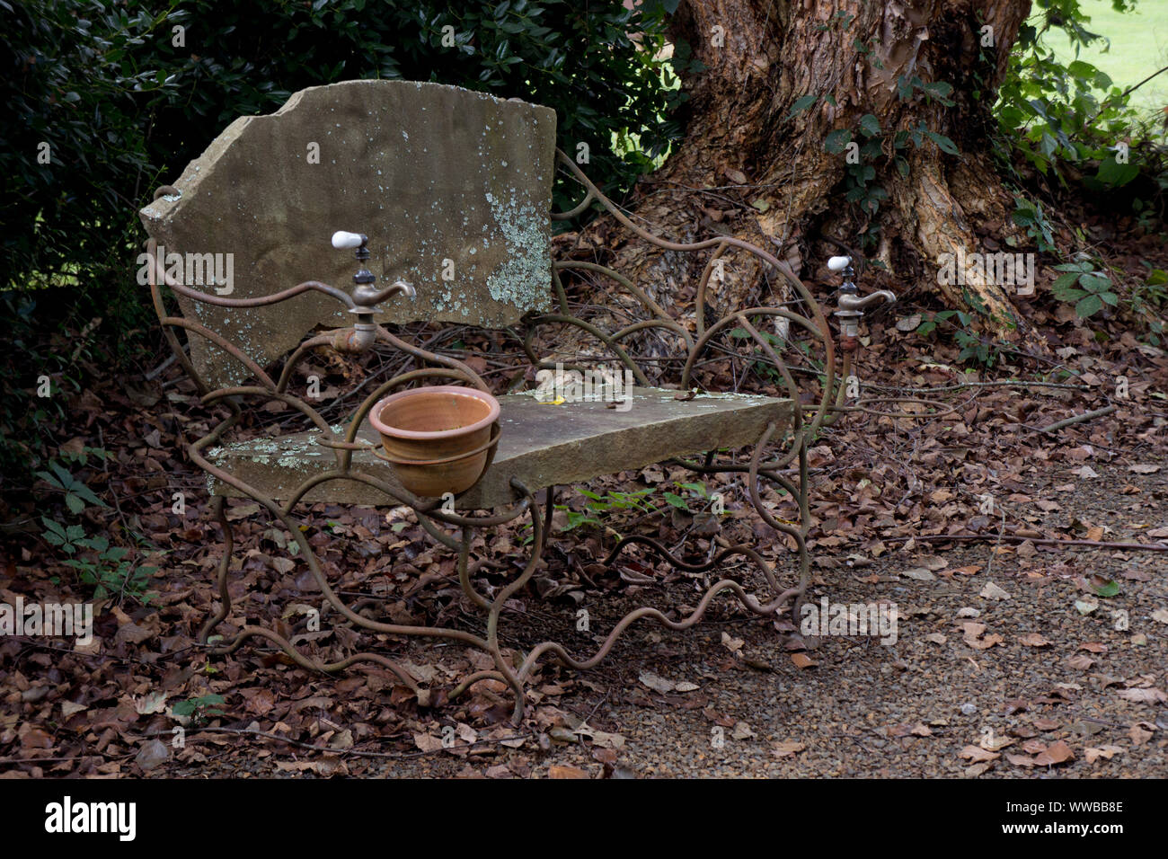 Handwerkliche Stein und schmiedeeisernen Bank unter einem alten Baum. Stockfoto