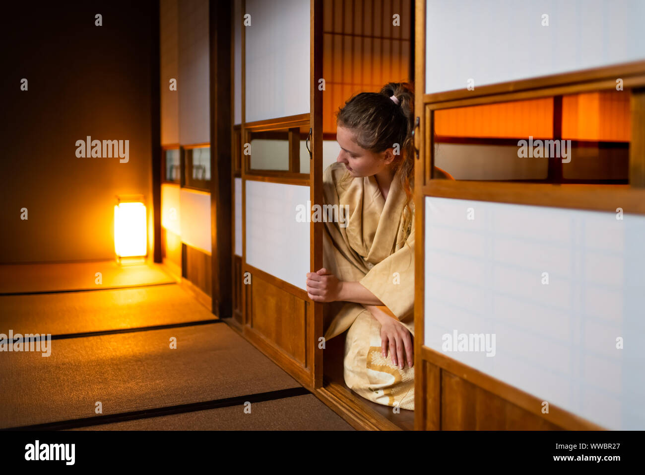 Die traditionellen japanischen Ryokan Zimmer mit Gaijin kaukasische Frau im Kimono, Tabi Socken Eröffnung shoji Schiebetüren Papier Türen sitzen auf Tatami Matten Boden Stockfoto