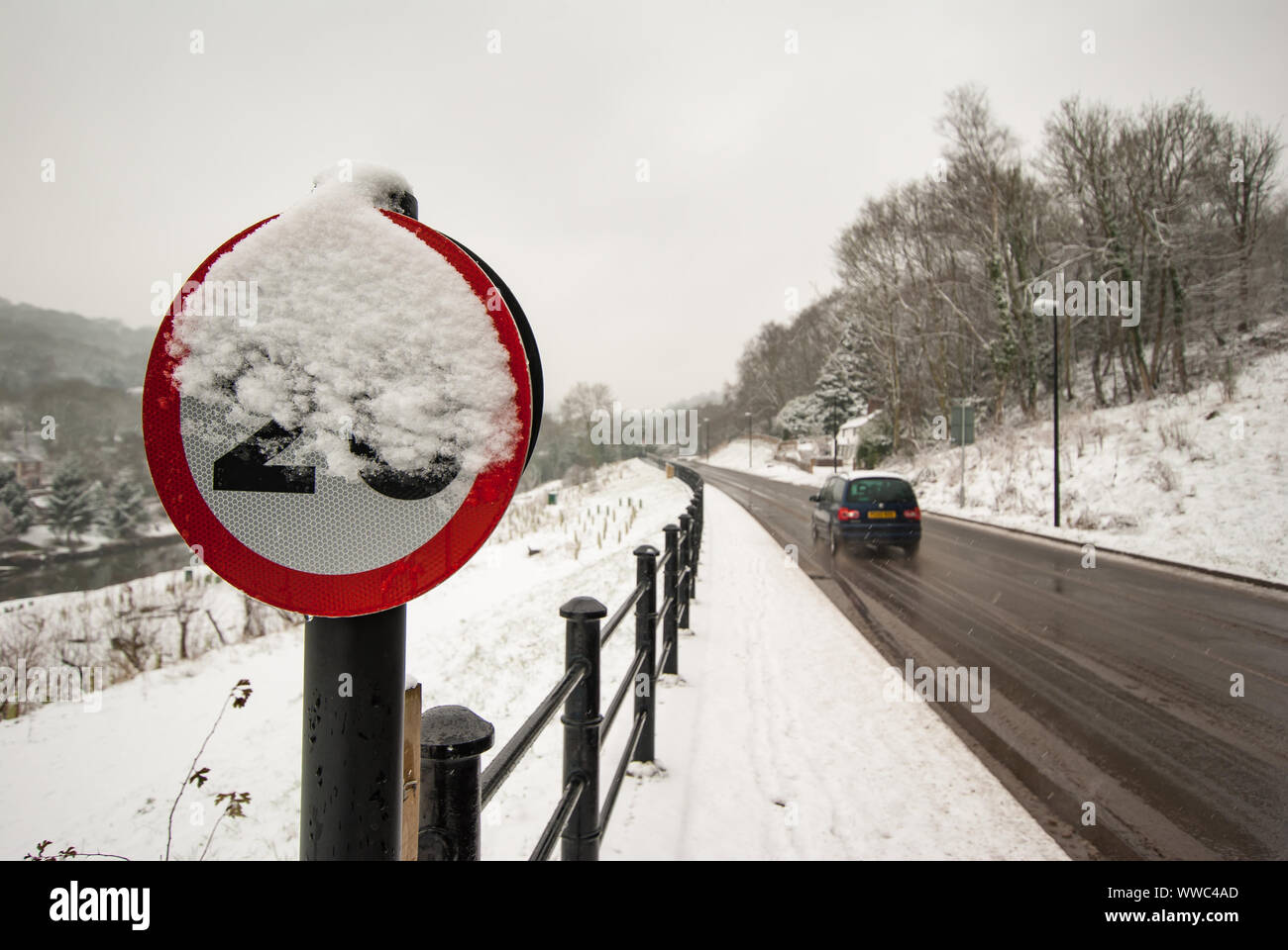 Tempolimit Zeichen teilweise verdeckt von Schnee als Car Geschwindigkeiten Vergangenheit auf rutschigem Untergrund. Stockfoto