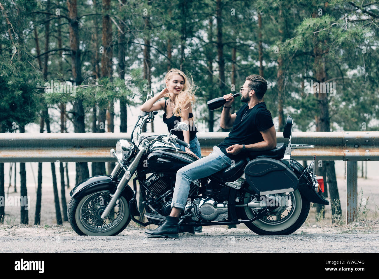 Junges Paar der Biker sitzen auf schwarzen Motorrad und man Alkohol trinken  aus der Flasche auf der Straße in der Nähe der grünen Wald Stockfotografie  - Alamy
