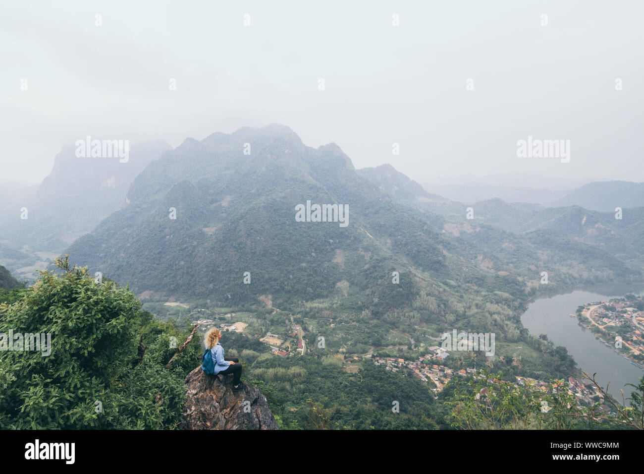 Junge kaukasier Frau steht oben auf dem Berg mit Blick auf das Flusstal in Nong Khiaw Dorf, Laos. Stockfoto Junge kaukasier Frau steht oben auf dem Berg mit Blick auf das Flusstal in Nong Khiaw Dorf, Laos. Stockfoto