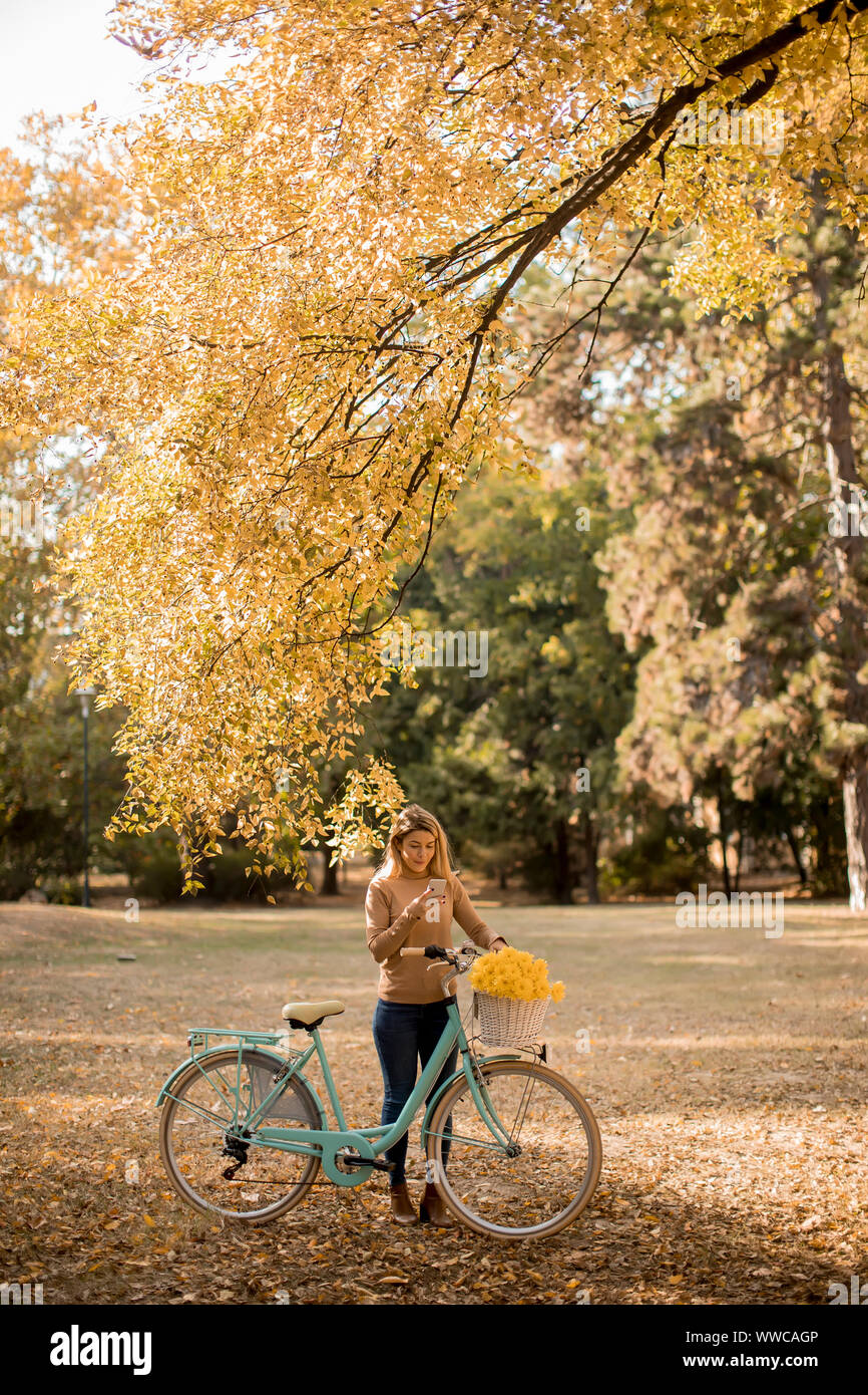 Hübsche, junge Frau mit dem Fahrrad über Smartphone im Herbst Park Stockfoto