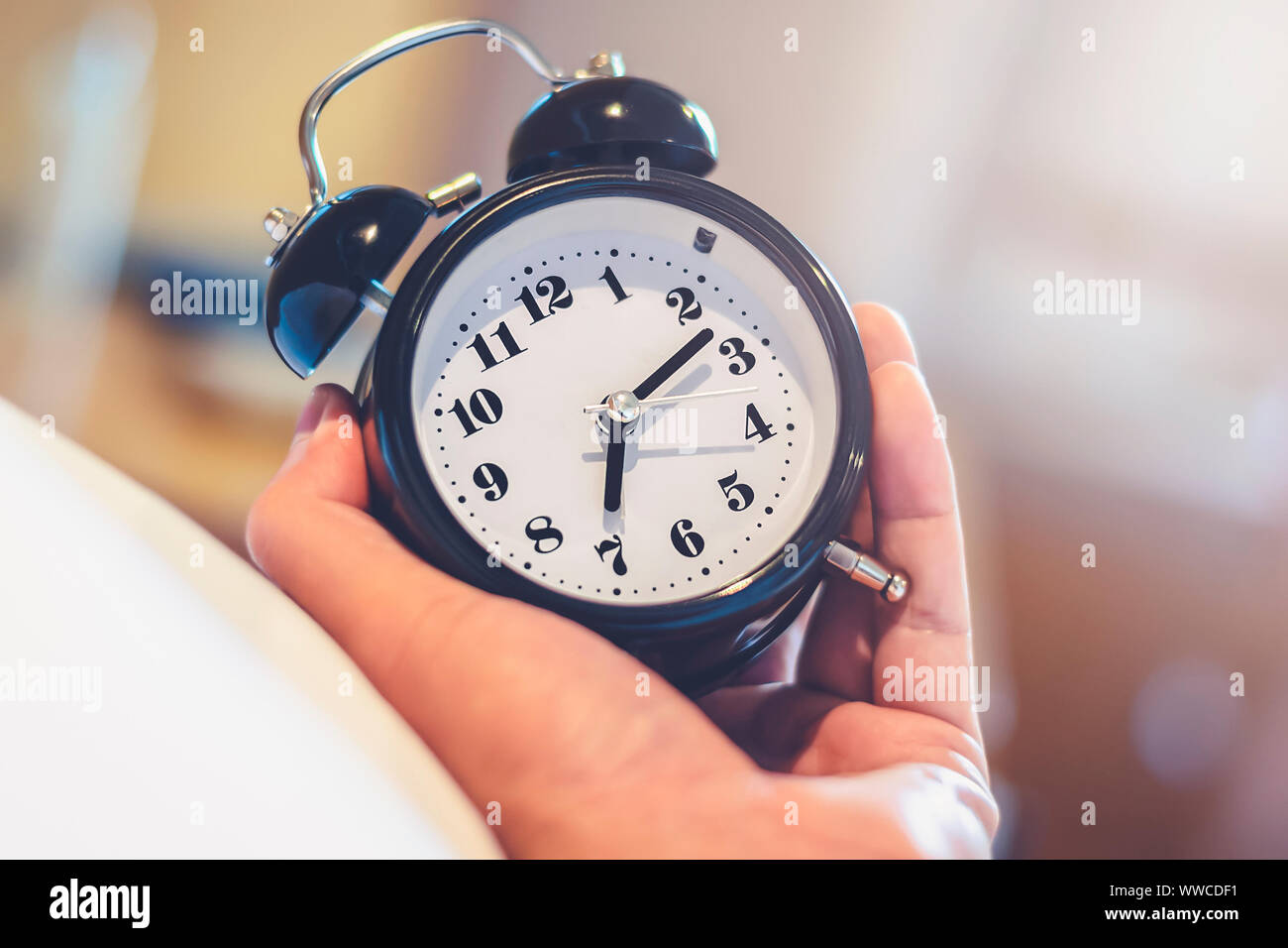 Mann hand Wecker zum Aufwachen um 7.00 Uhr morgens Aufwachen mit Licht im Schlafzimmer warm Vintage Style Stockfoto