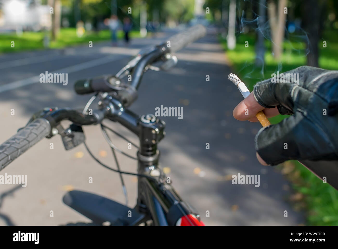 Eine Zigarette in der Hand eines rauchen Radfahrer, Fahrten mit dem Fahrrad auf dem Hintergrund der asphaltierte Weg des City Park Stockfoto