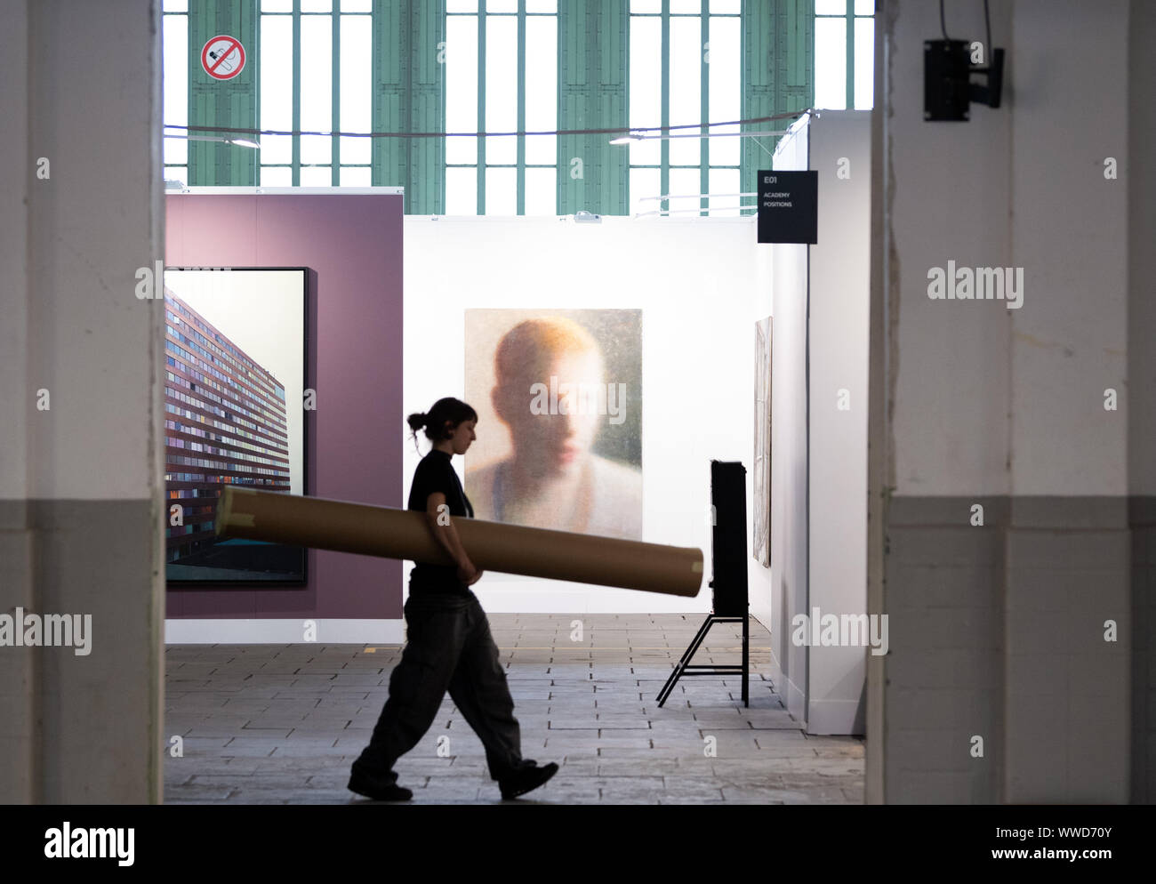 Berlin, Deutschland. 12 Sep, 2019. Während der Pressekonferenz für die Kunstmesse 'Positionen Berlin Art Fair" im Hangar 4 des Flughafen Tempelhof, eine Frau geht über die Gemälde "Das Gebäude" (Öl auf Leinwand von Jens Hausmann (l) und "Untitled" (Öl, Acryl und Pigmente auf Leinwand) von Robert Bosisio. Die Messe findet vom 12. bis 15. 09.2019. 70 internationale Galerien sind eingeladen worden, ihre wichtigsten Werke der zeitgenössischen und modernen Kunst während der Berliner Kunst Woche zu präsentieren. Credit: Soeren Stache/dpa-Zentralbild/ZB/dpa/Alamy leben Nachrichten Stockfoto