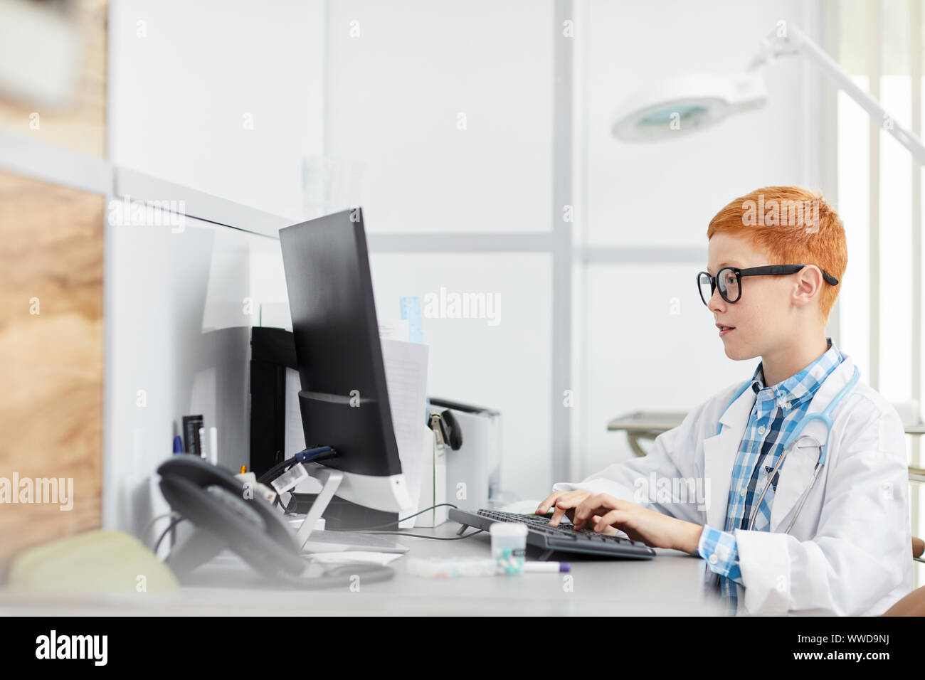 Seitenansicht Portrait von niedlichen Rothaarigen Junge spielt Doktor am Schreibtisch im Büro sitzen und mit Computer, kopieren Raum Stockfoto