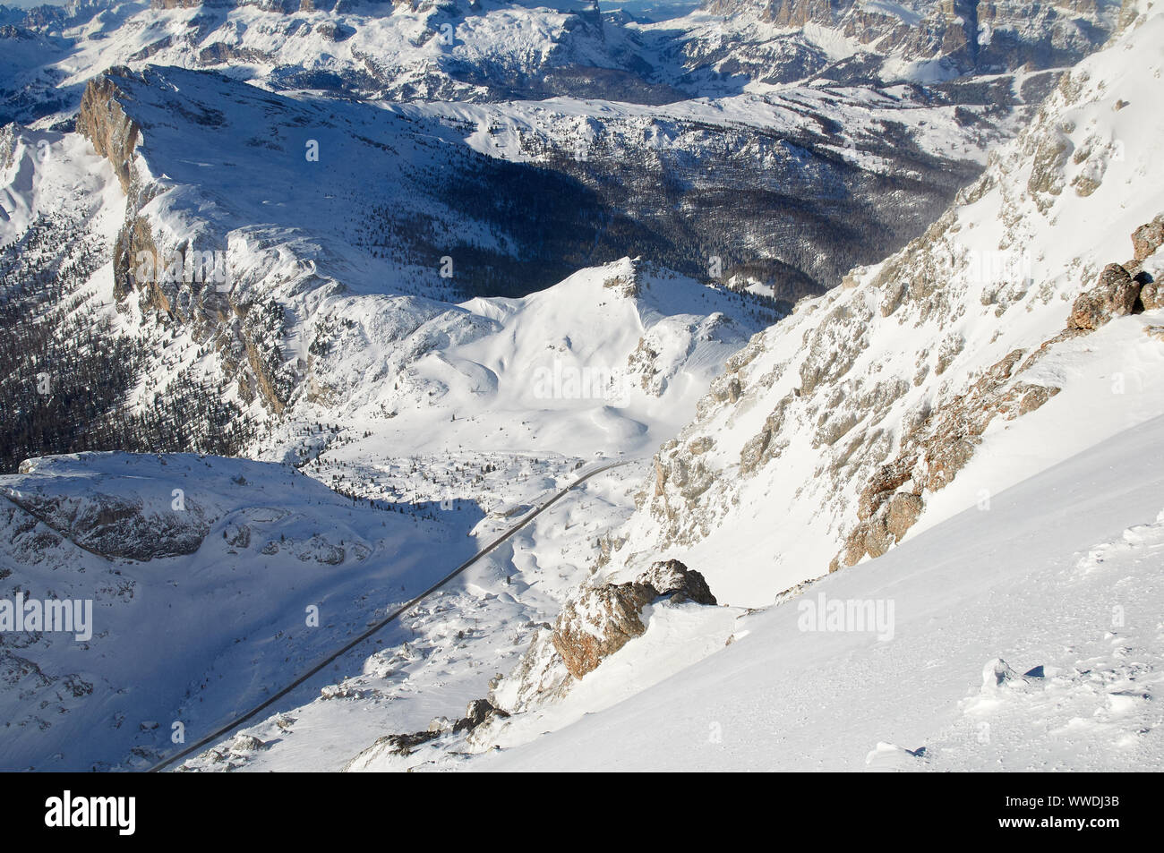 Panoramablick vom Berg Lagazuoi auf der Straße zum Valparola Pass zwischen den verschneiten Bergen, mit einem einzigen Bus auf der Passstraße. Stockfoto