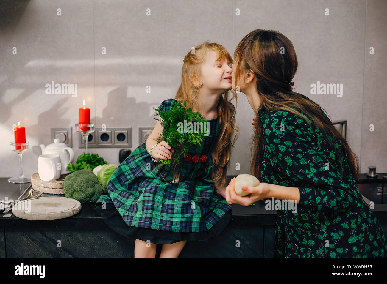 Schöne Mutter mit Tochter. Familie arbeitet in der Küche. Zwei Damen in einem grünen Kleid Stockfoto