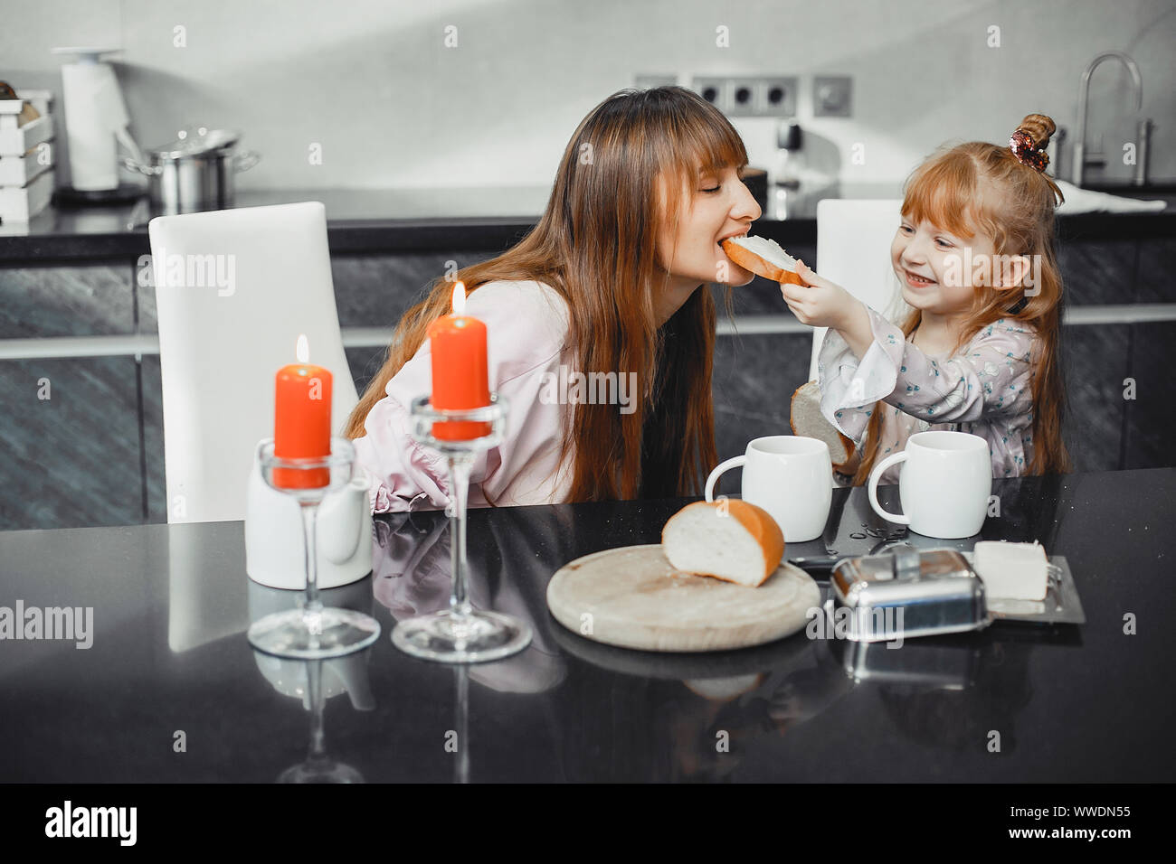 Schöne Mutter mit Tochter. Familie in der Küche sitzt. Cute gitl Brot essen Stockfoto