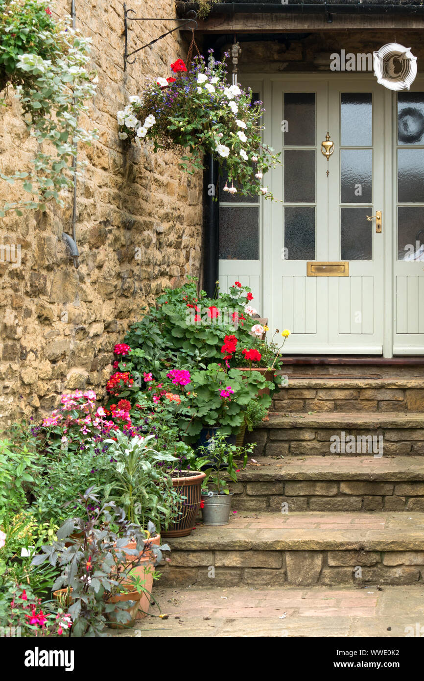 Ziemlich Steinstufen, die vordere Tür mit Pflanzmaschinen, hängende Körbe und blühenden Pflanzen zu Haus, Easton auf dem Hügel, Northamptonshire, England, Großbritannien Stockfoto