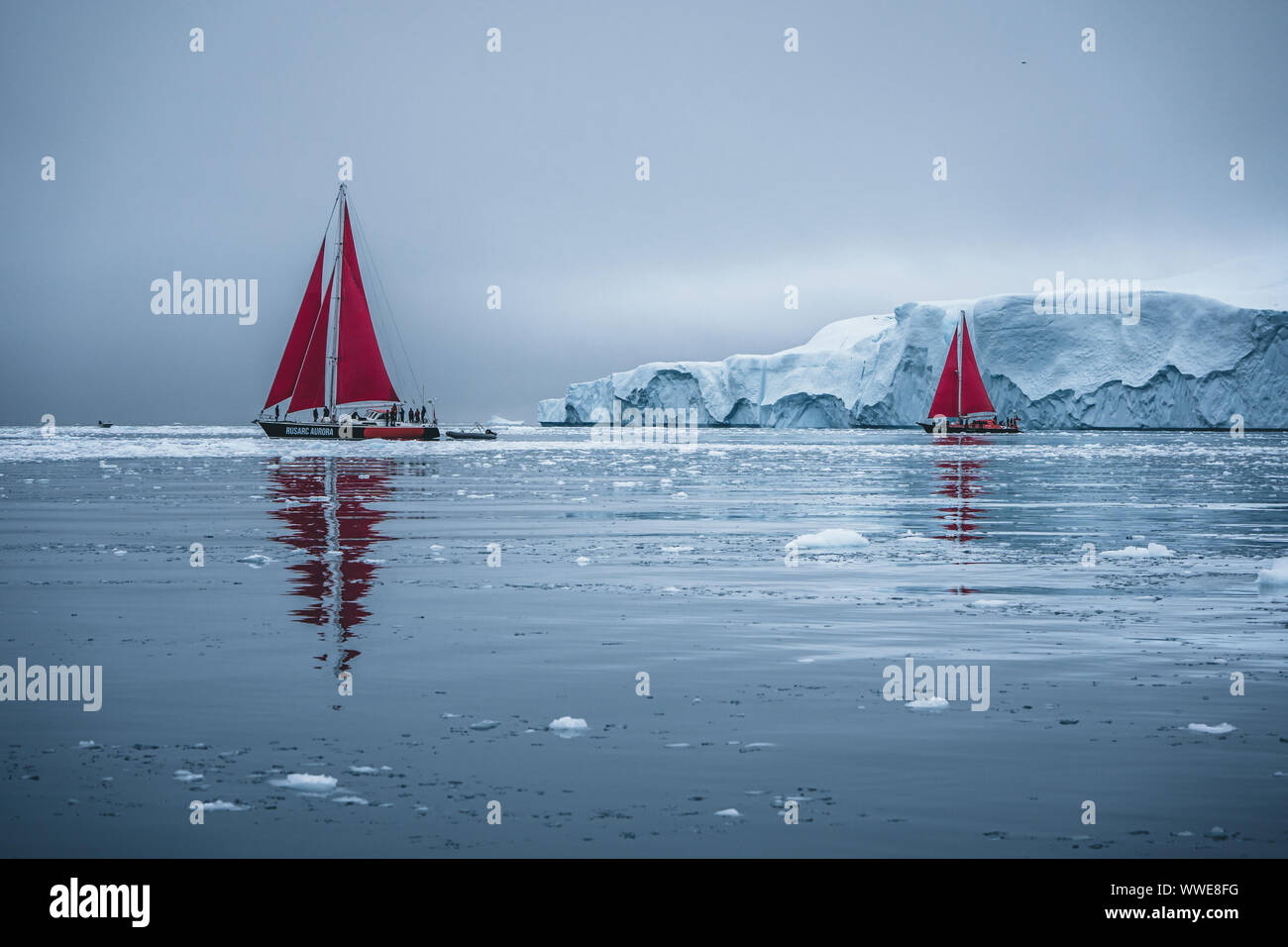 Schöne rote Segelboot in der nächsten zu einem massiven Eisbergs zeigt die Skala Arktis. Kreuzfahrt unter schwimmende Eisberge in der Diskobucht Gletscher Stockfoto