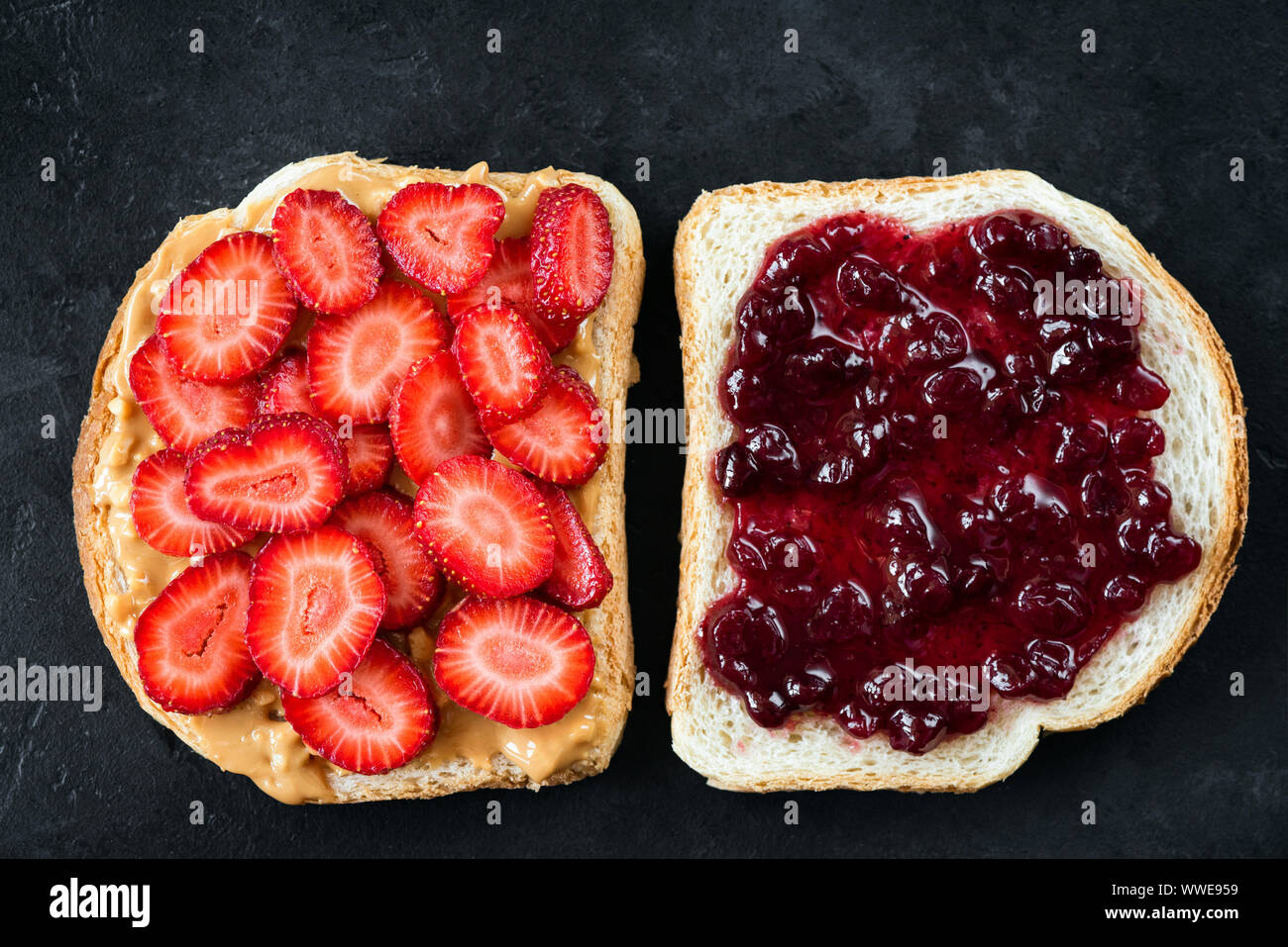 Peanut Butter und Marmelade Sandwich Alternative. Sandwich mit Erdnussbutter und frische Erdbeeren und klassische Marmelade Toast auf schwarzem Hintergrund, Ansicht von oben Stockfoto