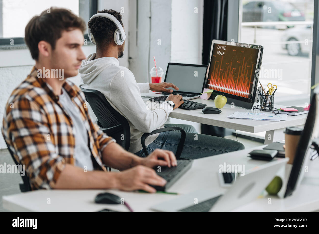 Rückansicht des afrikanischen amerikanischen Programmierer mit Computer mit online Handel auf dem Monitor in der Nähe von Kollege im Büro Stockfoto