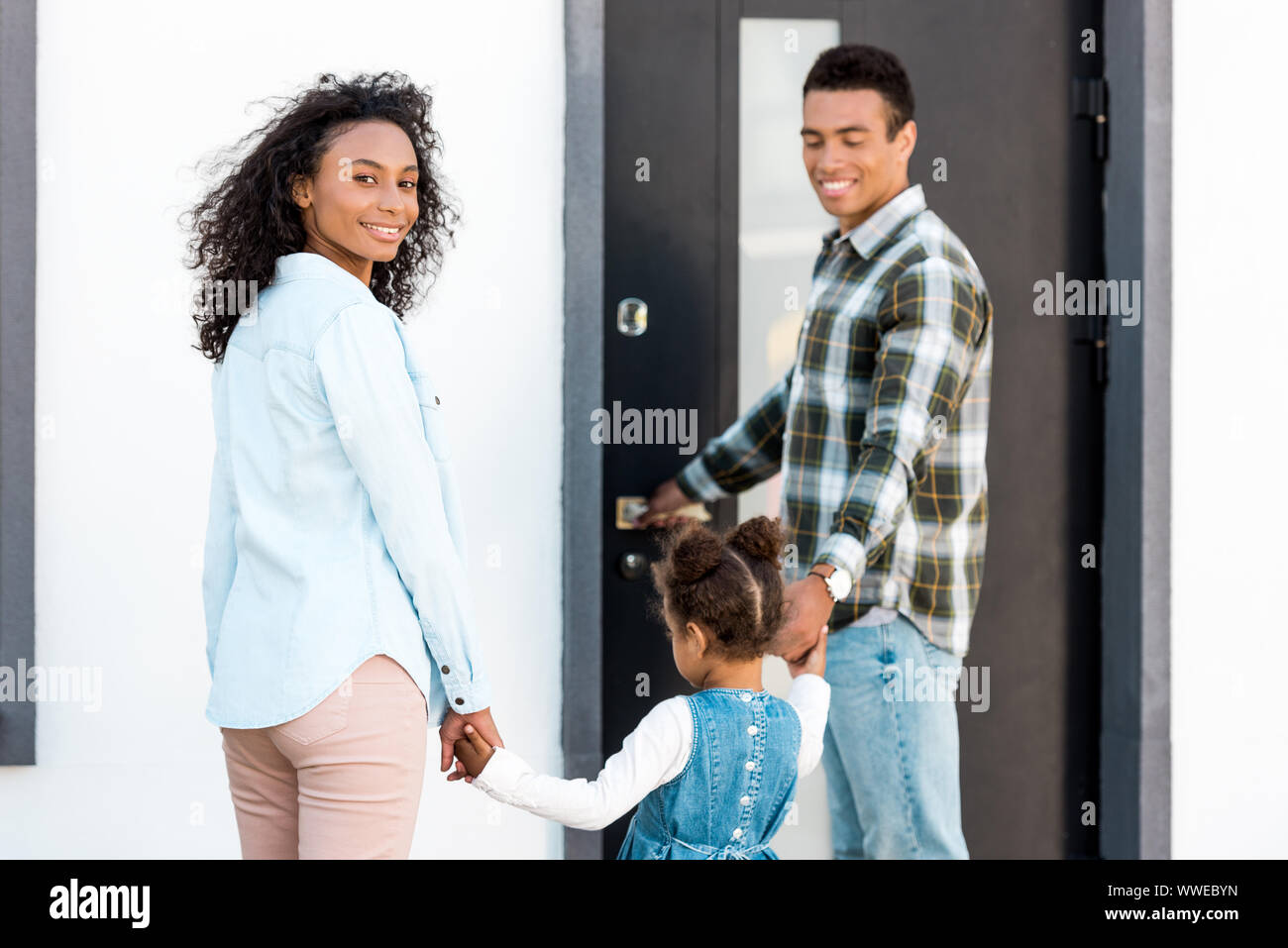 Familie, die in der Nähe von neuen Haus, während Vater Hände mit Kind und Mutter an der Kamera auf der Suche Stockfoto