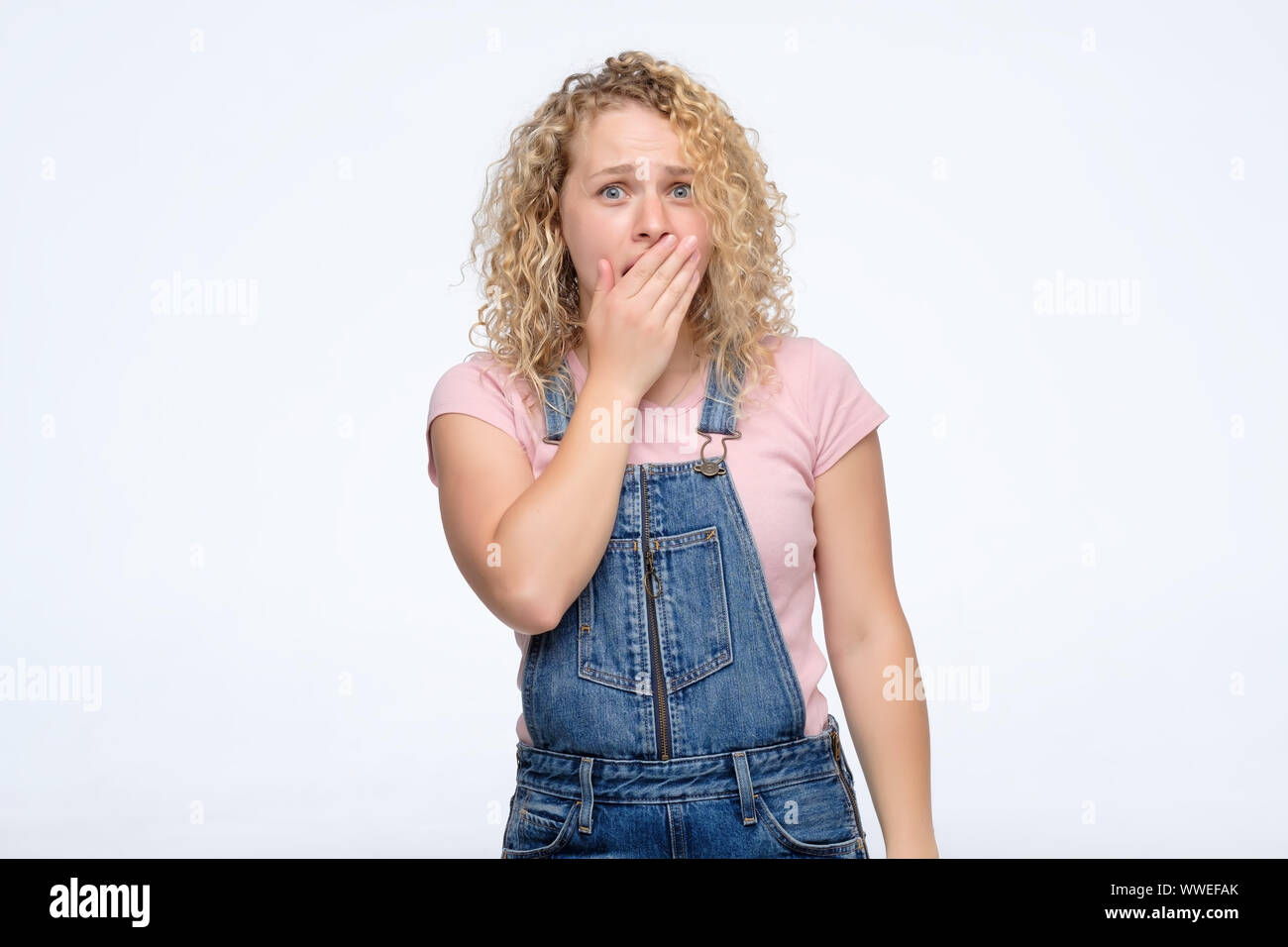 Leger gekleidete junge Lockige Frau mit ihrem Mund in der Überraschung. Studio shot Stockfoto