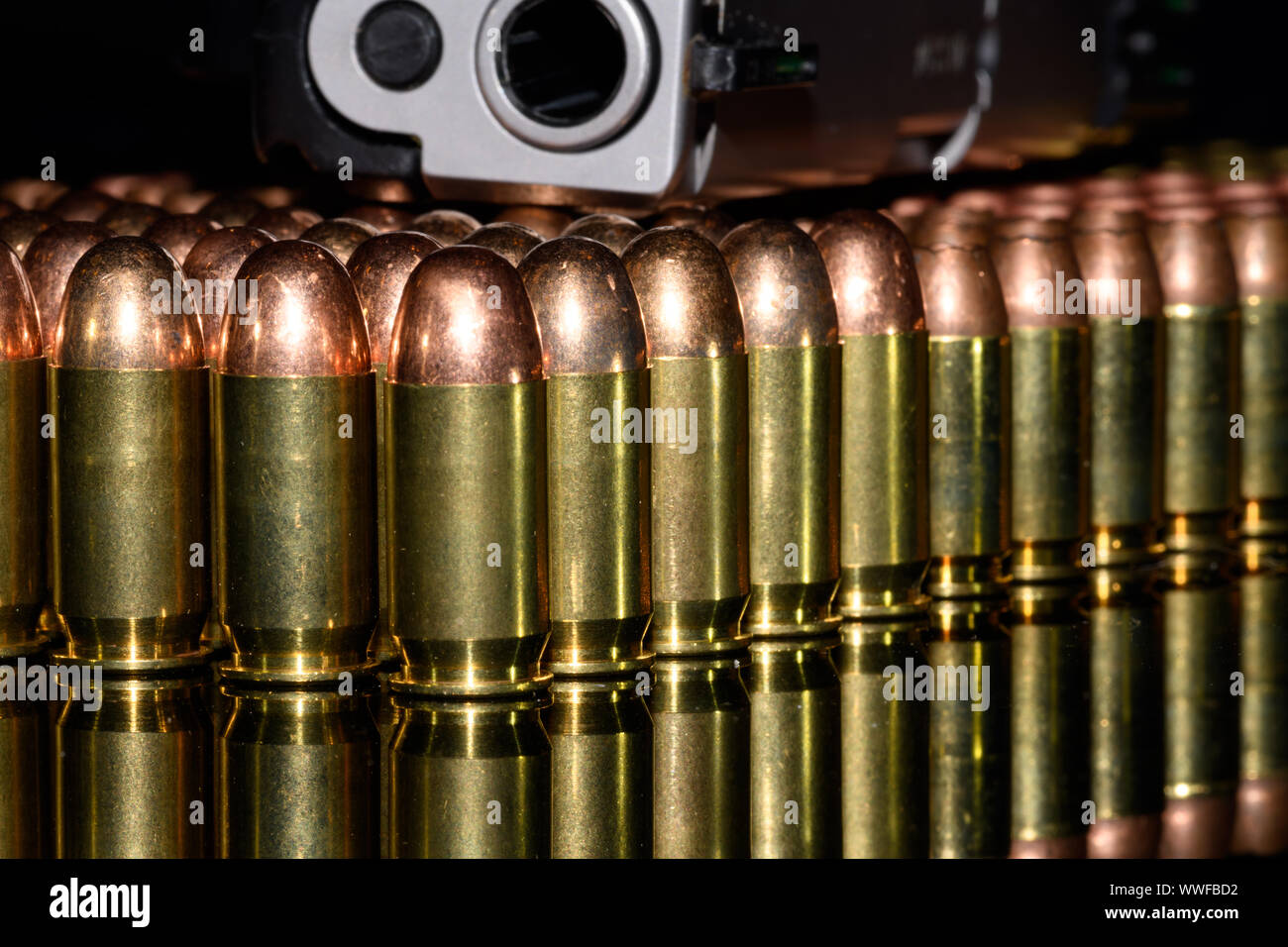 Halbautomatische Pistole auf Reihen von Munition, Munition mit schwarzem Hintergrund und Reflexion Stockfoto