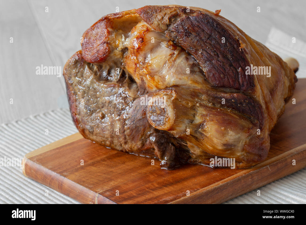 Gebratene Lammkeule ruht auf einem hölzernen Schneidebrett und Unterlage. Graues Holz Hintergrund Stockfoto