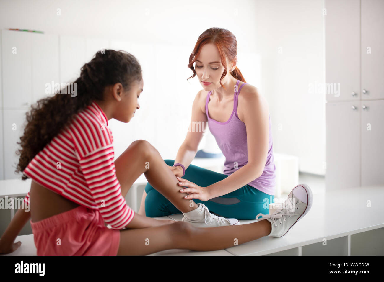 Rothaarige PE Lehrer helfen Mädchen mit Knie Trauma Stockfoto