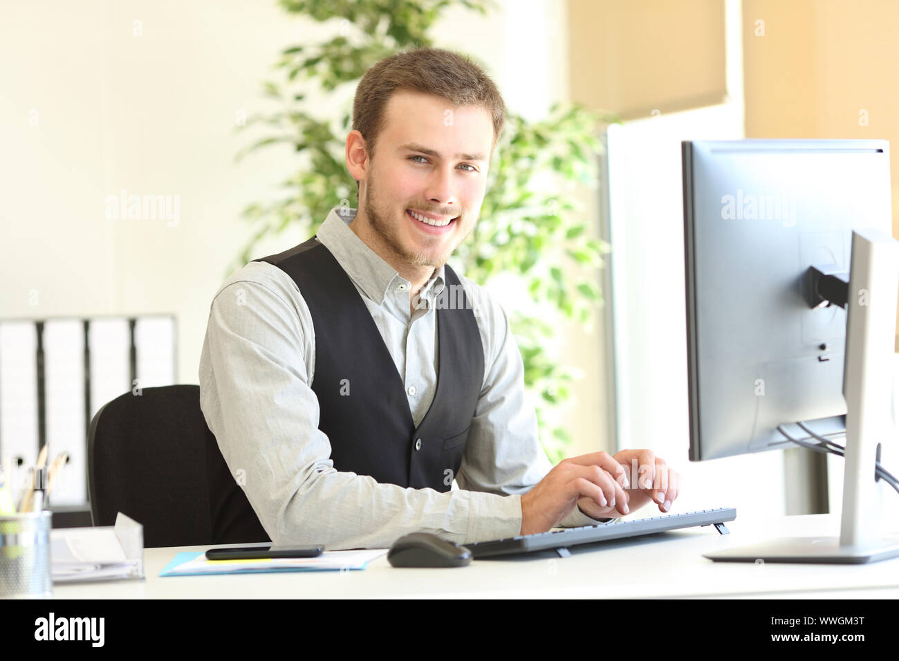 Happy executive posiert an Kamera suchen mit den Händen auf der Tastatur des Computers im Büro Stockfoto