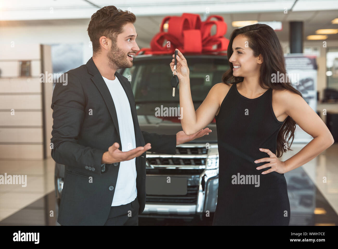 Junge schöne Frau präsentiert nagelneues Auto zu ihr überrascht stattlicher Mann in der Händlerniederlassung center Stockfoto