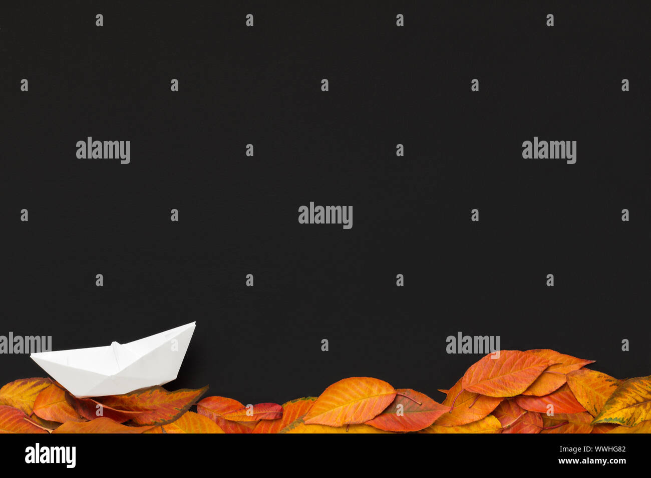 Segeln Papier Schiff auf Laub auf schwarzem Hintergrund Stockfoto