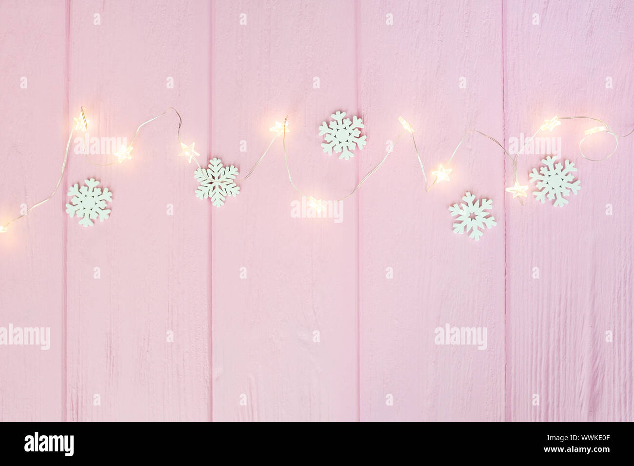 Weihnachtsbeleuchtung Girlande mit Schneeflocken Grenze über rosa Holz Hintergrund. Im