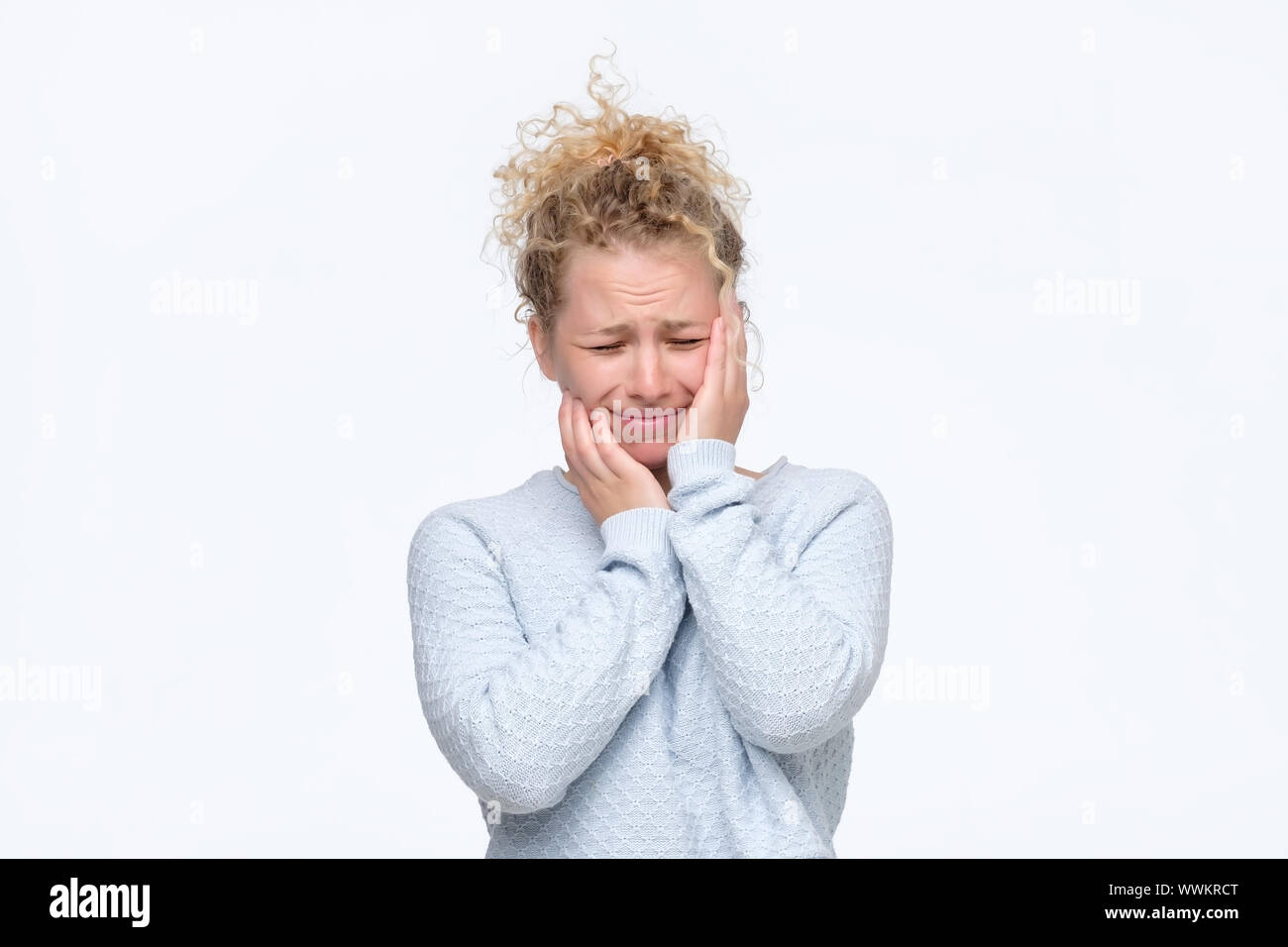 Frustrierte junge blonde lockige Frau in Blau Pullover in schreckliche Kopfschmerzen die Hände auf den Kopf finsteres Gesicht mit Schmerzen. Studio shot Stockfoto