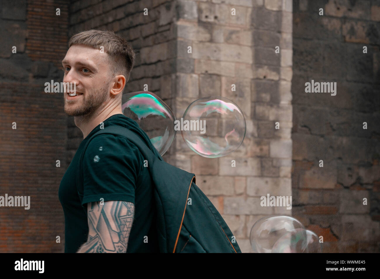Attraktive lächelnden Mann mpassing durch Seifenblasen an der alten, spanischen Stadt. Travel Blogger. Europäische Urlaub voller Lachen und Glück. Stockfoto