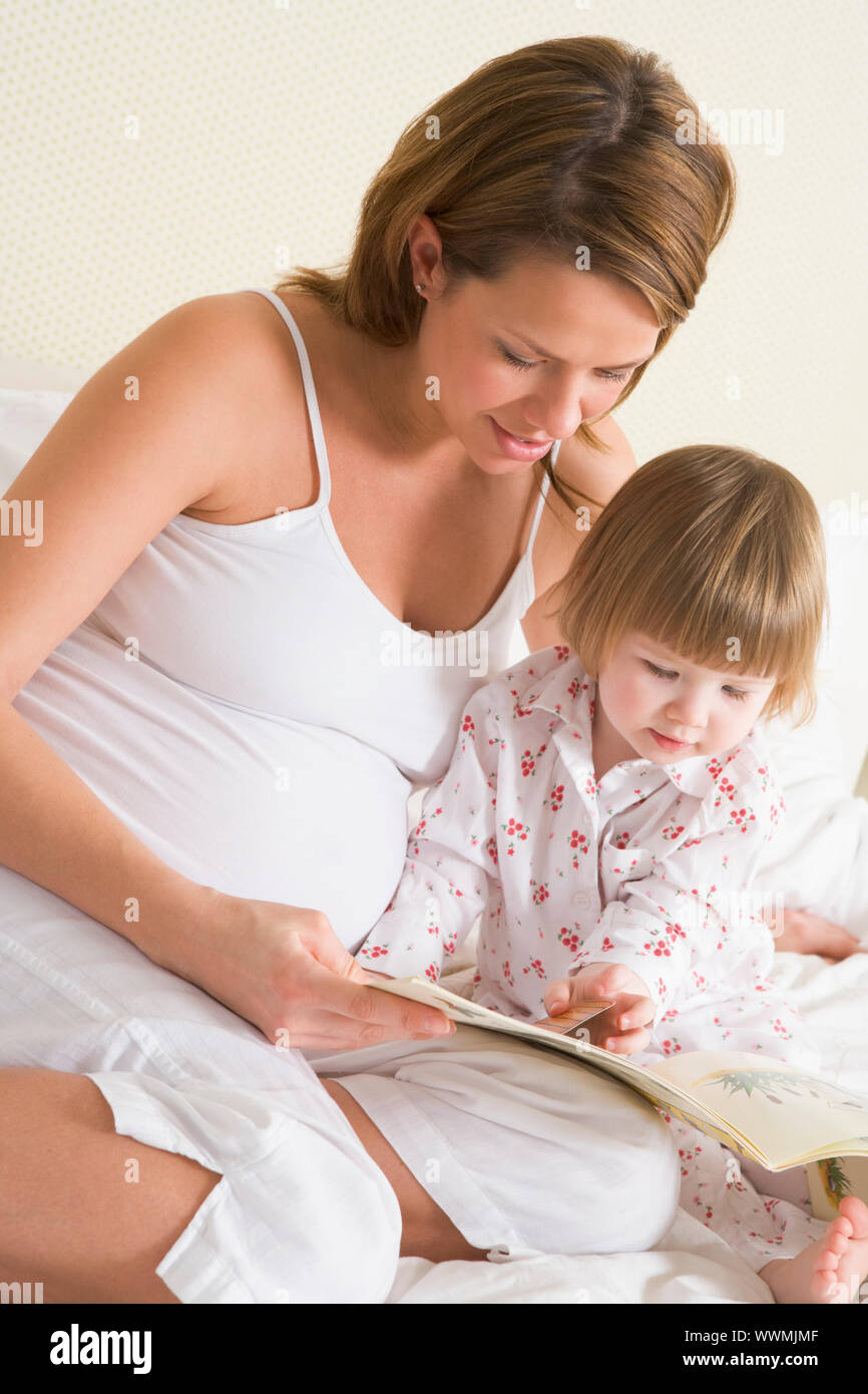 Schwangere Frau im Schlafzimmer Lesebuch mit Tochter Stockfoto