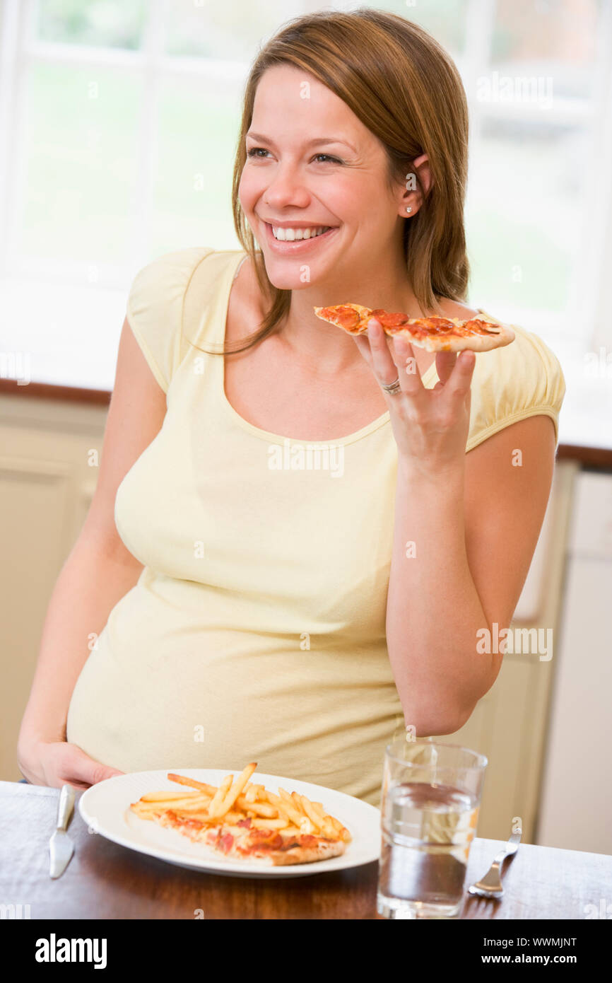 Schwangere Frau in der Küche Essen, Pommes Frites und Pizza lächelnd Stockfoto