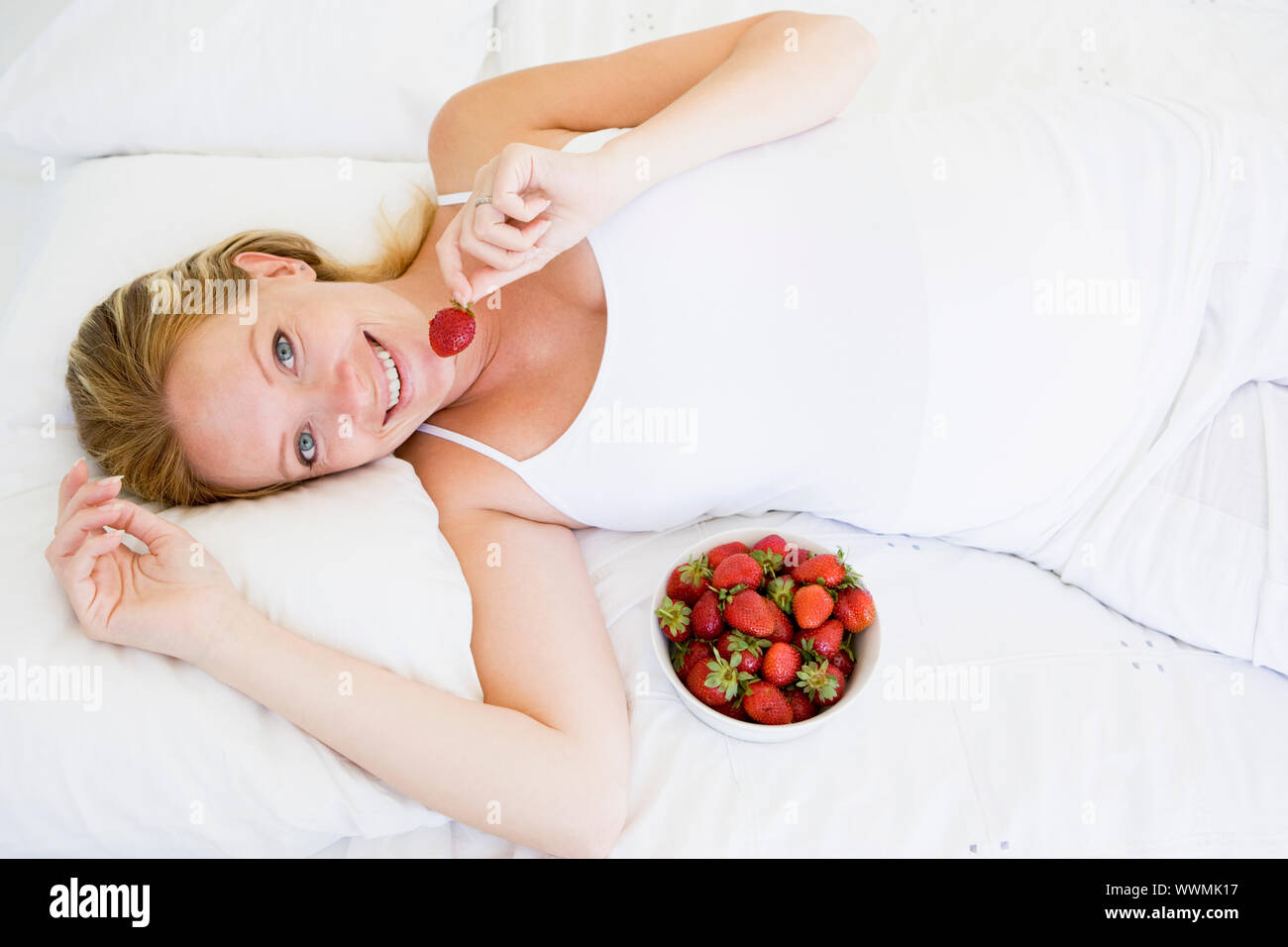 Schwangere Frau im Bett mit Schale Erdbeeren lächelnd Stockfoto