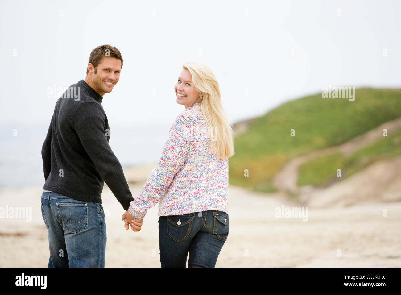 Paare, die am Strand Hand in Hand lächelnd Stockfoto