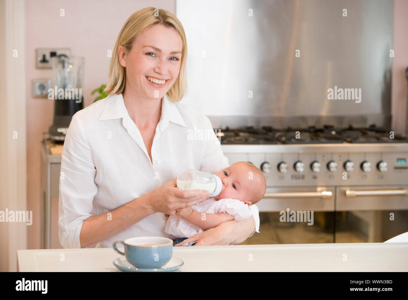 Fütterung Baby in Küche mit Kaffee lächelnden Mutter Stockfoto