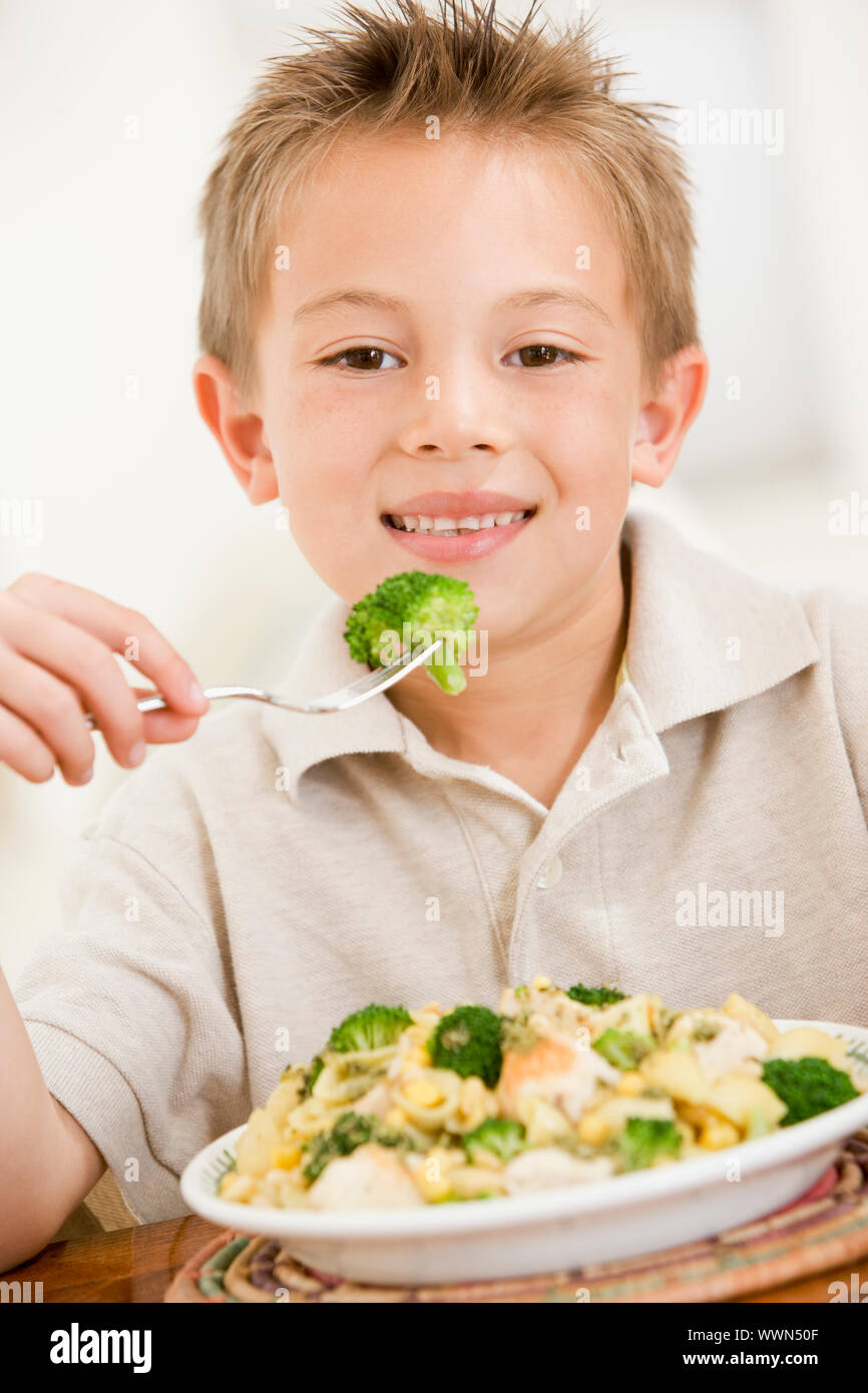 Kleiner Junge drinnen essen Nudeln mit Brokkoli lächelnd Stockfoto