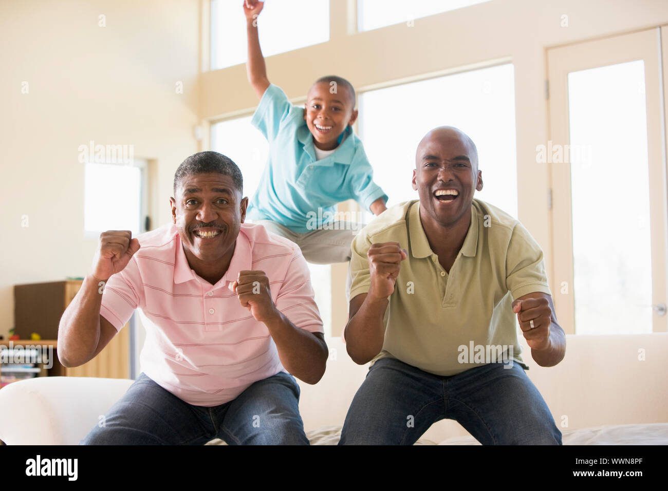 Zwei Männer und jungen im Wohnzimmer jubeln und lachen Stockfoto