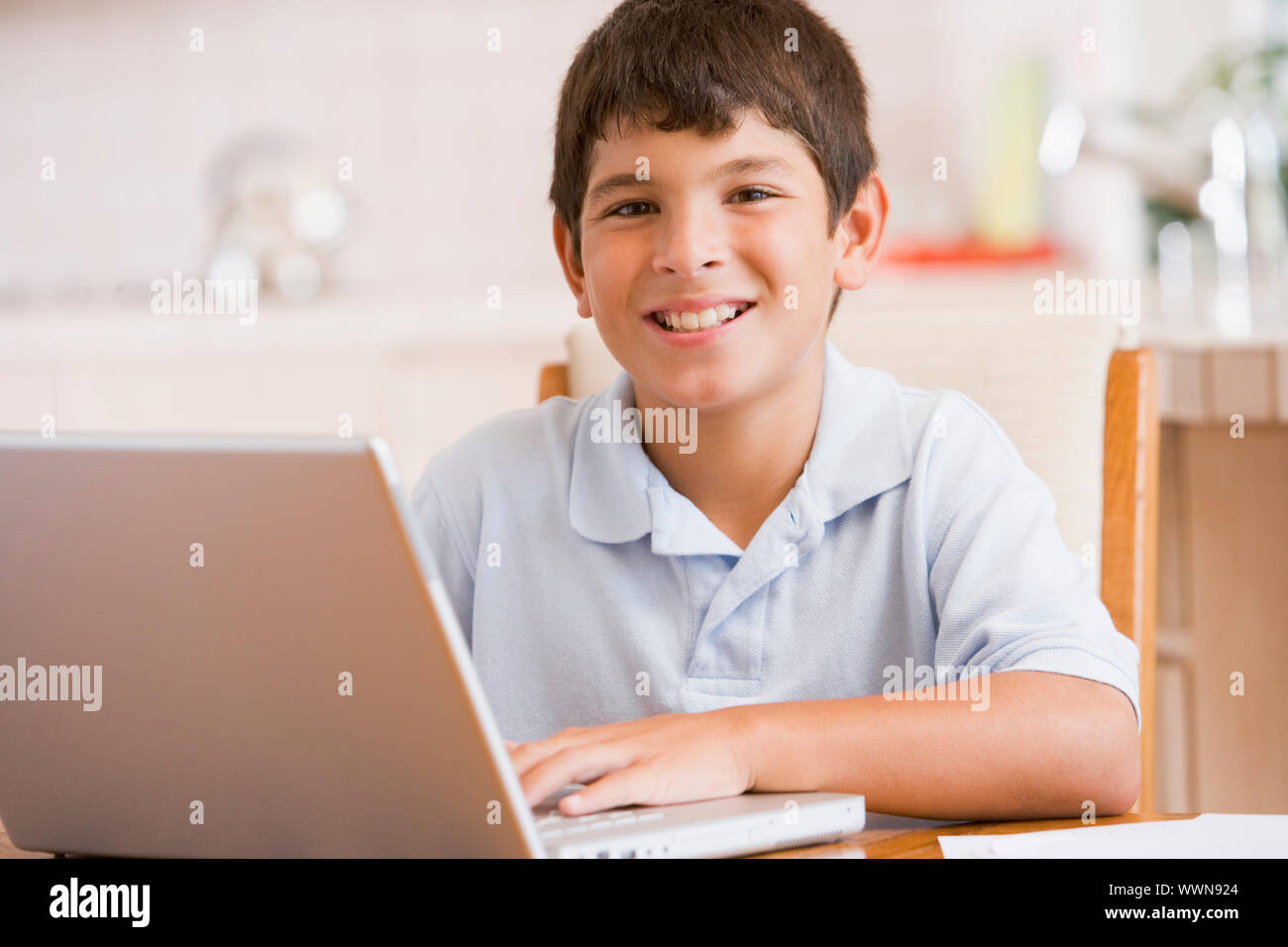 Kleiner Junge in Küche mit Laptop und Papierkram lächelnd Stockfoto