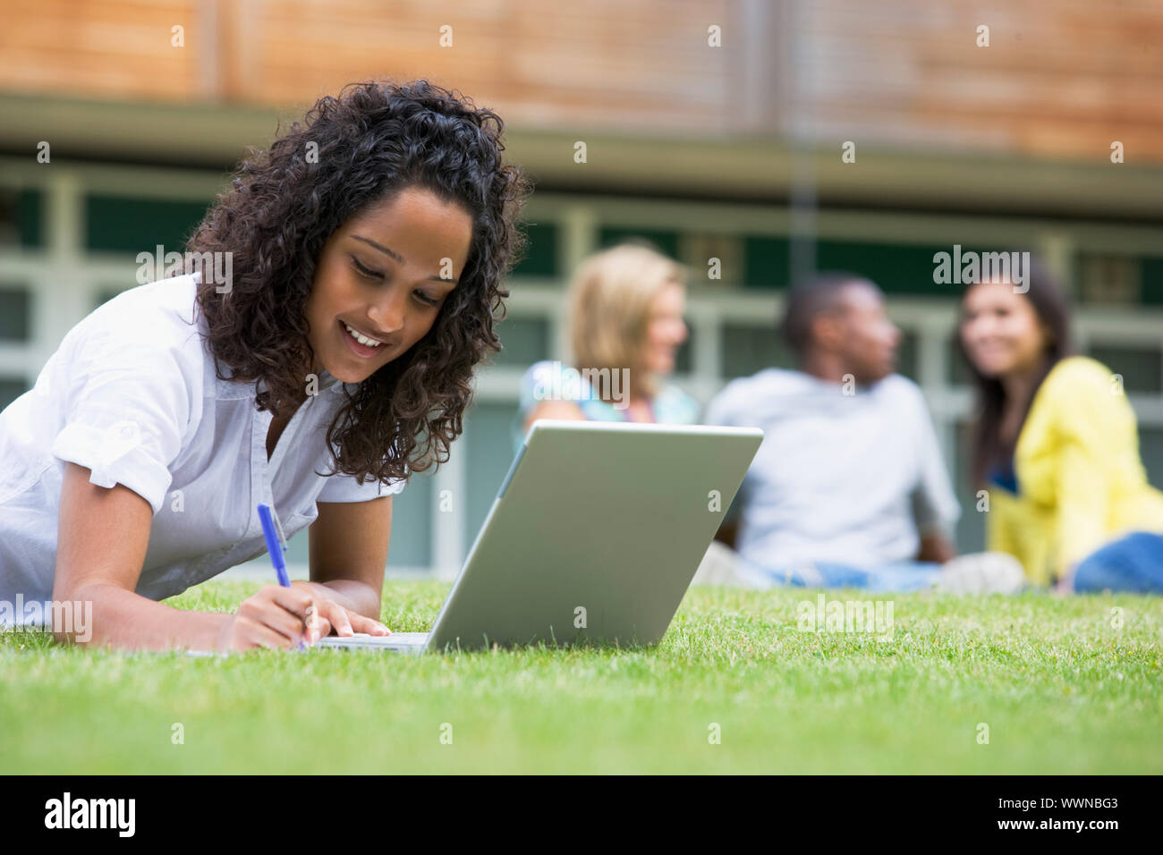 Junge Frau mit Laptop auf dem Campus Rasen, mit anderen Studenten Stockfoto