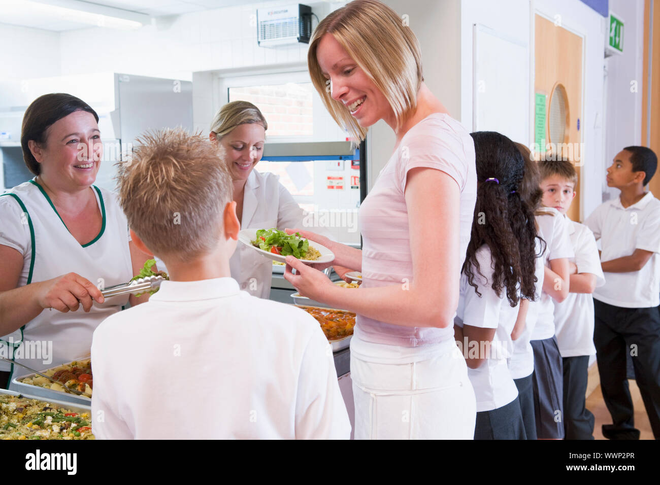 Schüler in der Cafeteria Schlange mit Lehrer zur Mittagszeit Stockfoto