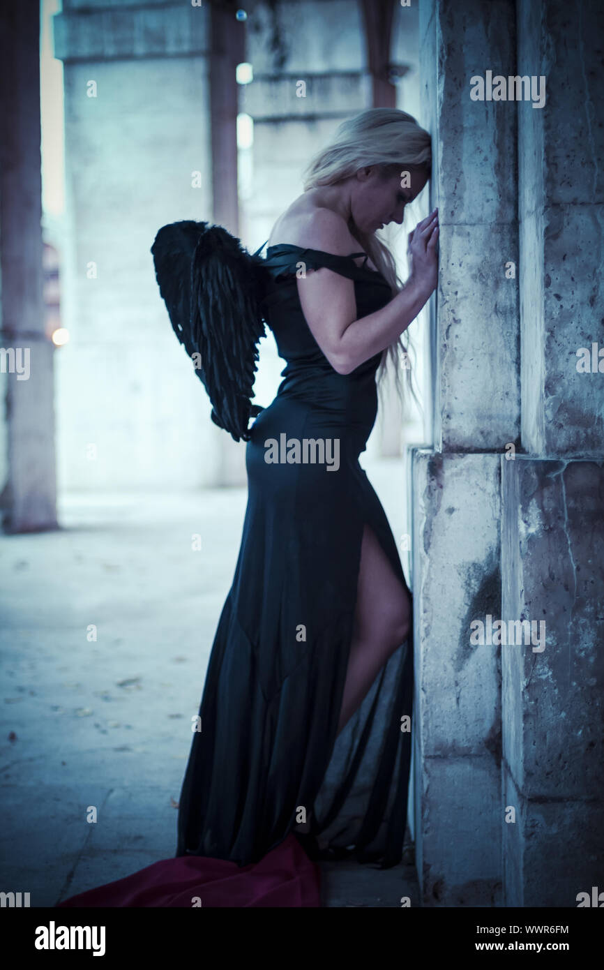 Ein Engel in der Stadt, schöne Blondine mit langen Haaren in Schwarz und mit schwarzen Flügeln gekleidet Stockfoto
