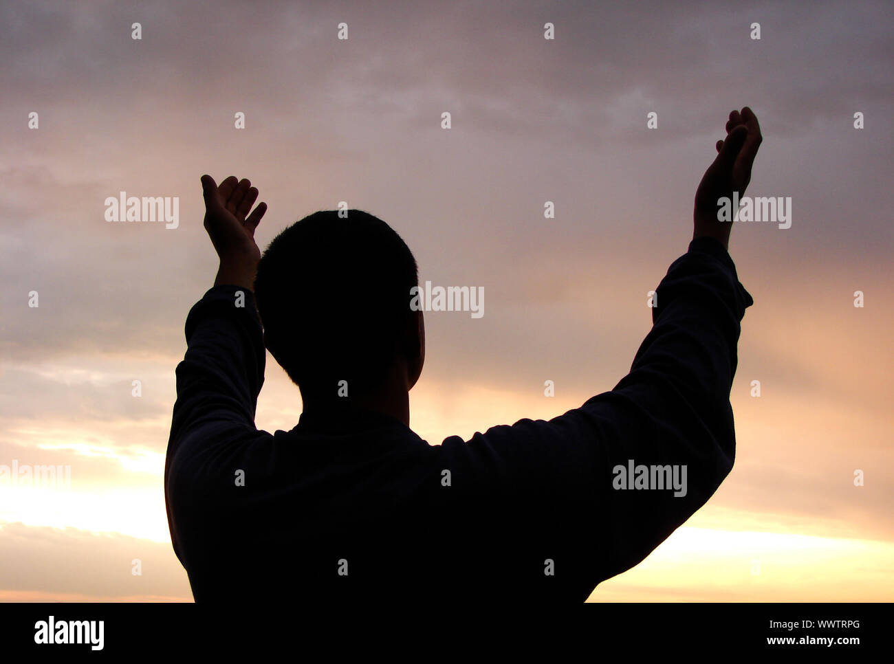 Ein Mann steht auf gegen eine Sonne mit gehievt, die Hände Stockfoto